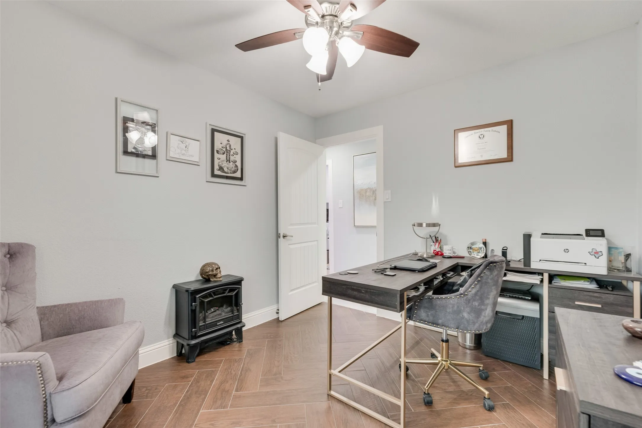 Home office with a wood stove, ceiling fan, and baseboards