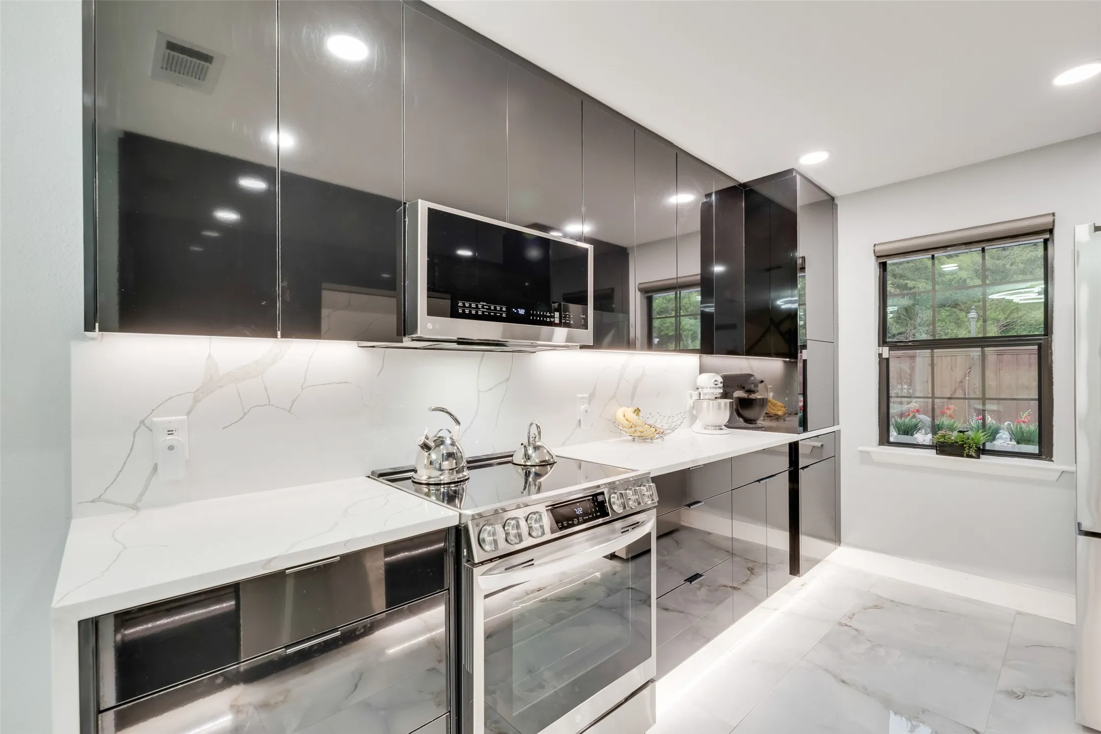 Kitchen with appliances with stainless steel finishes, modern cabinets, light stone countertops, light marble finish floors, and baseboards