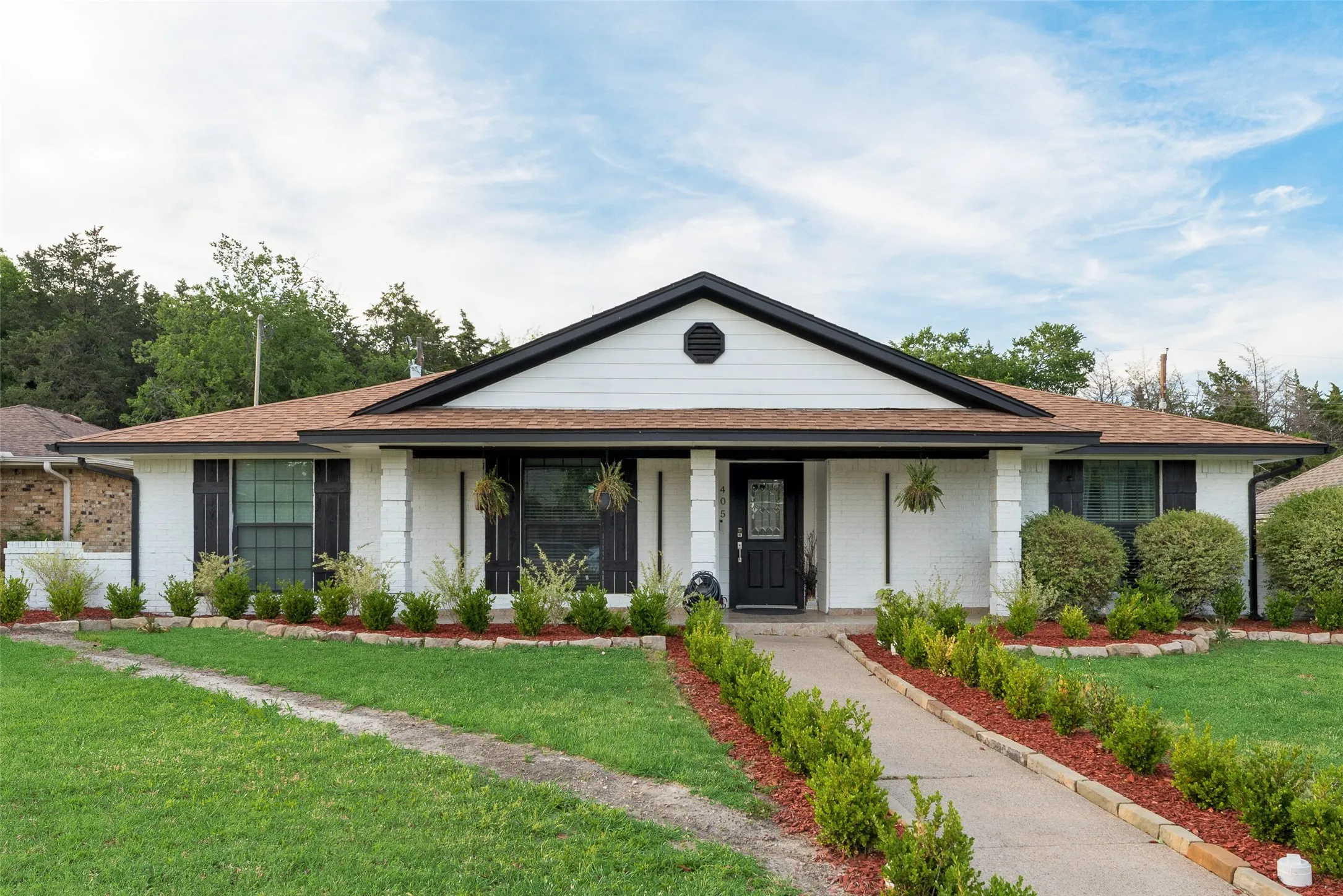 Ranch-style home with brick siding, a front lawn, roof with shingles, and covered porch