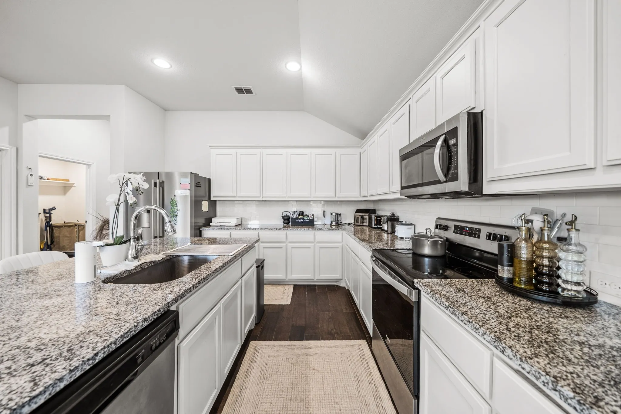 Spacious kitchen featuring white cabinetry, granite countertops, stainless steel appliances, a kitchen island with an undermount sink, and recessed lighting