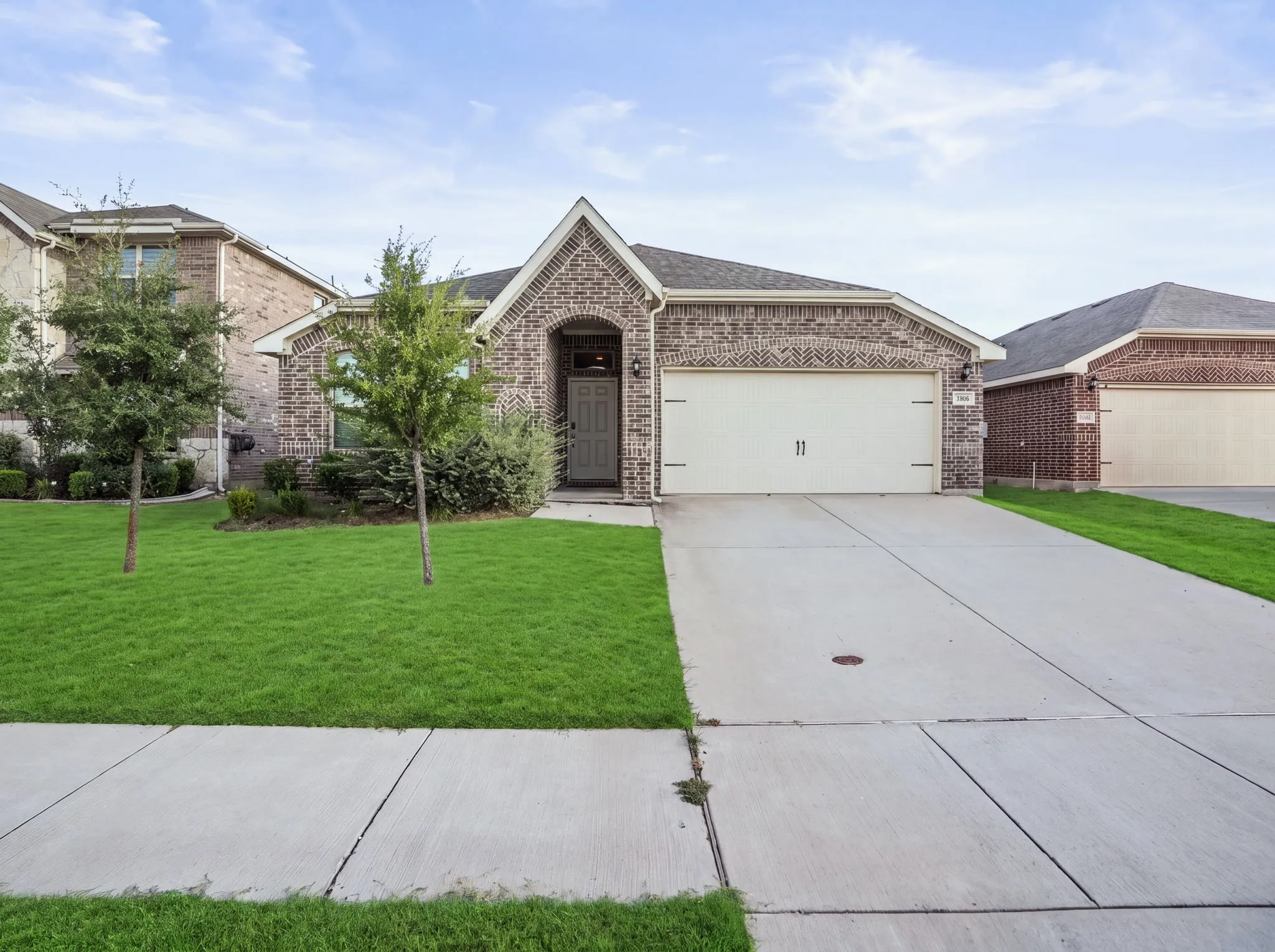 Brick exterior with an arched entryway, attached two-car garage, concrete driveway, and front lawn