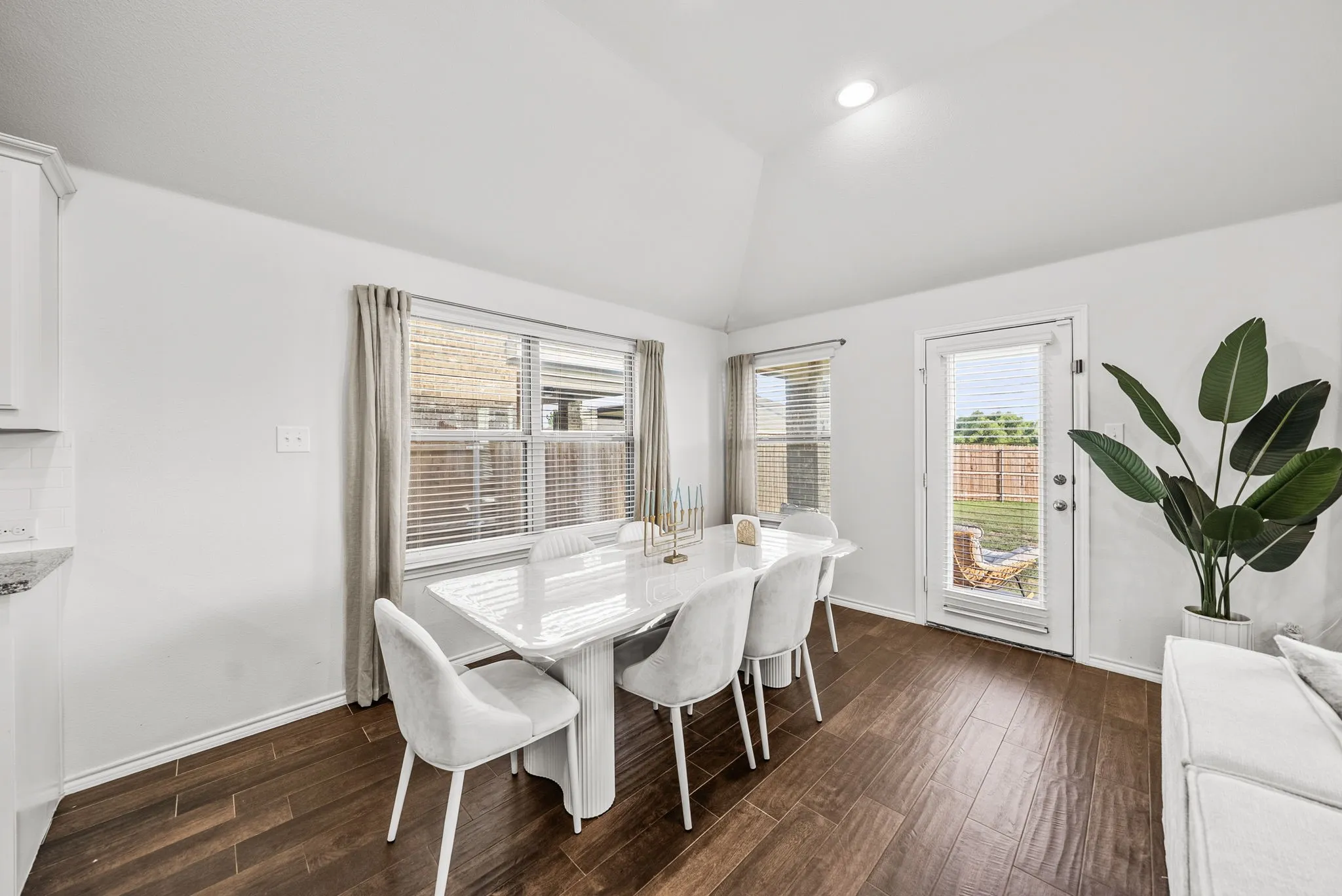 Vaulted ceiling, wood-finish flooring, white walls, multiple windows with blinds, and a glass-paneled exterior door