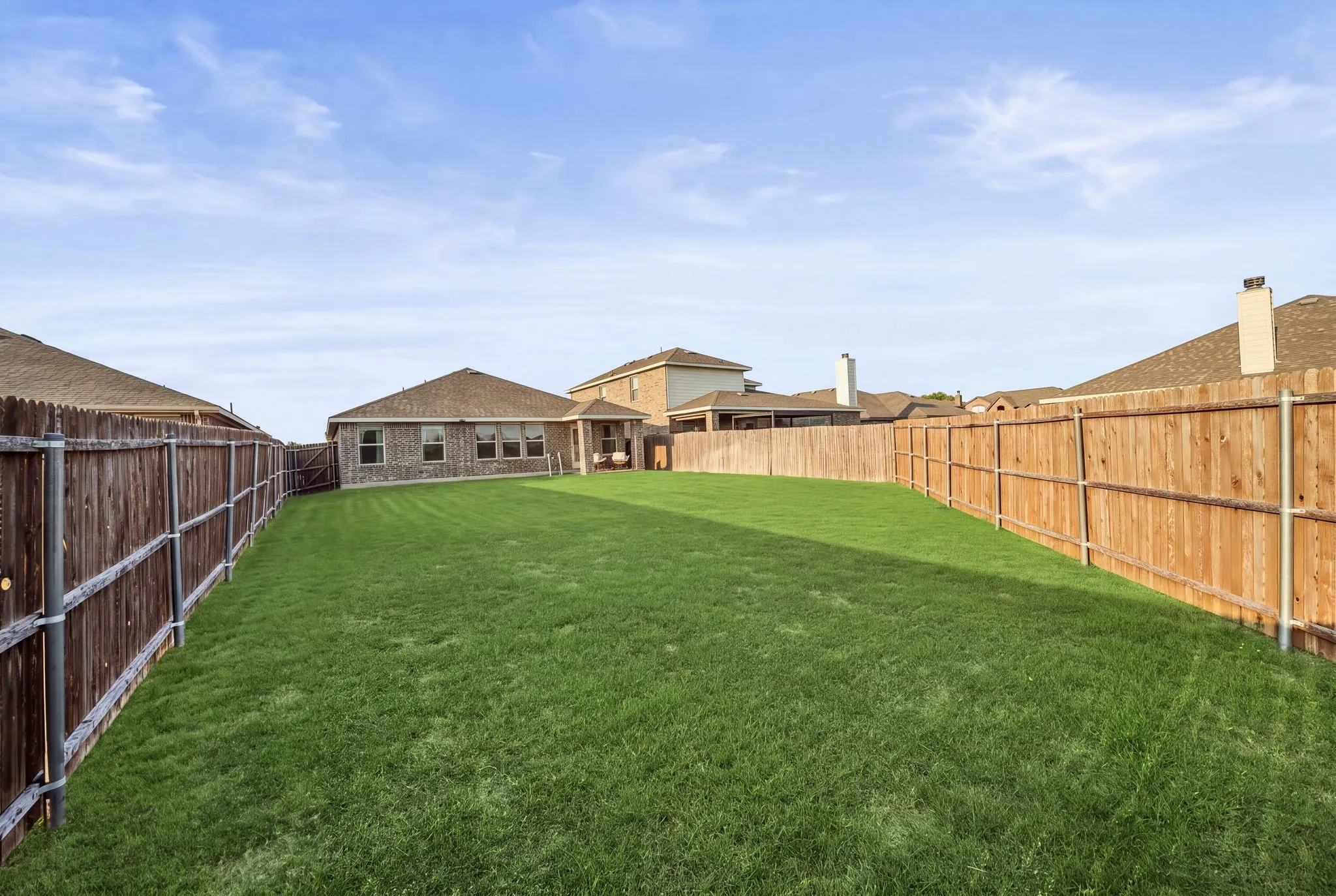 Expansive backyard featuring a large grass area, wood privacy fencing, and a rear structure with multiple windows