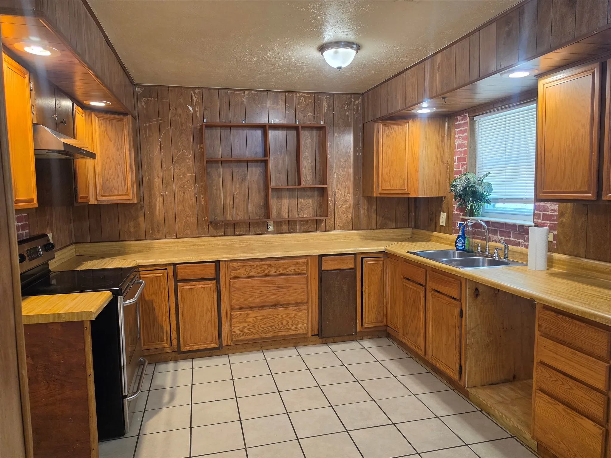 Kitchen featuring wood cabinetry, laminate countertops, a stainless steel sink, a range, and tile flooring