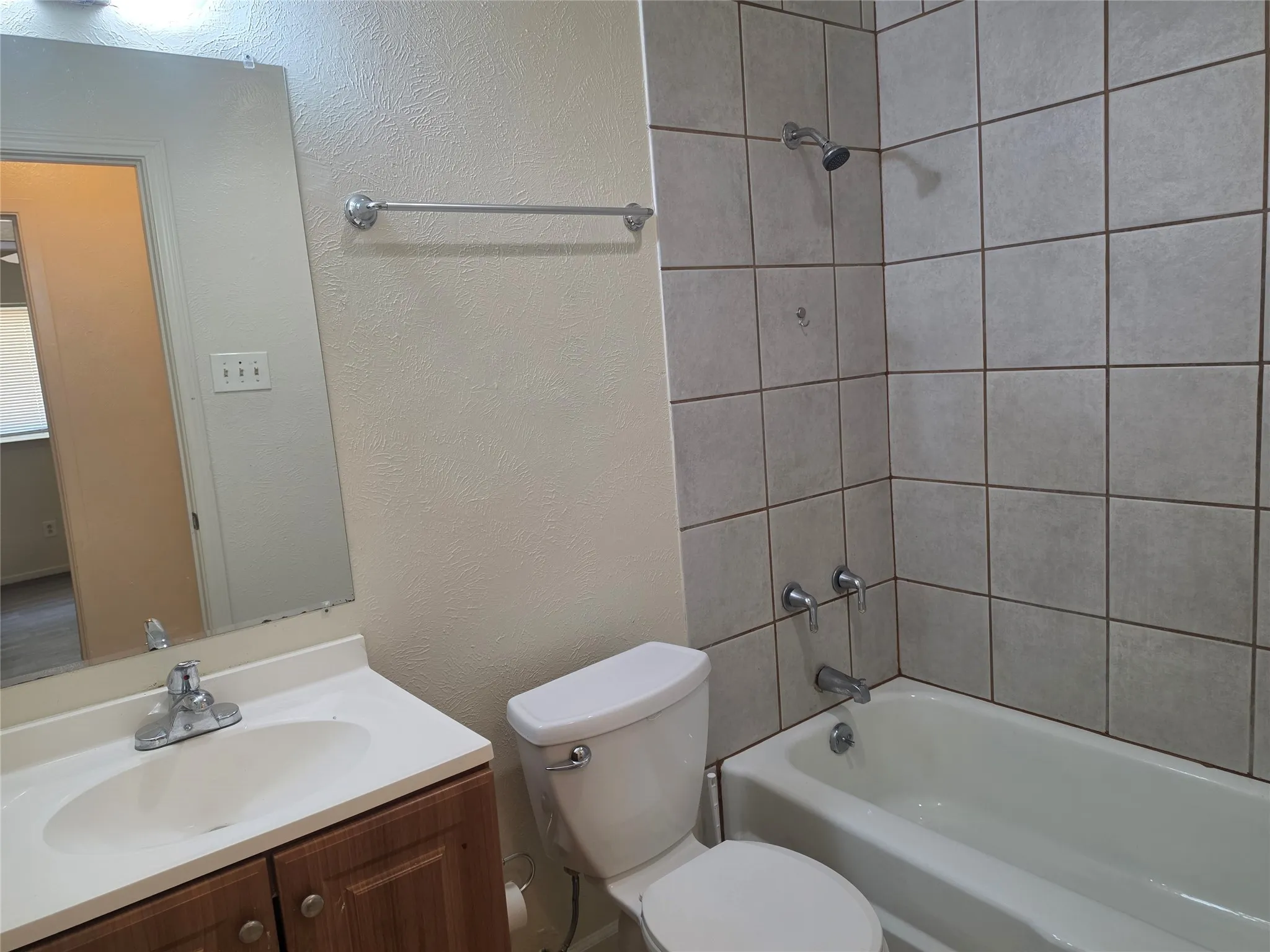 Bathroom featuring a vanity with a laminate countertop, toilet, and a shower/tub combination with ceramic tile surround