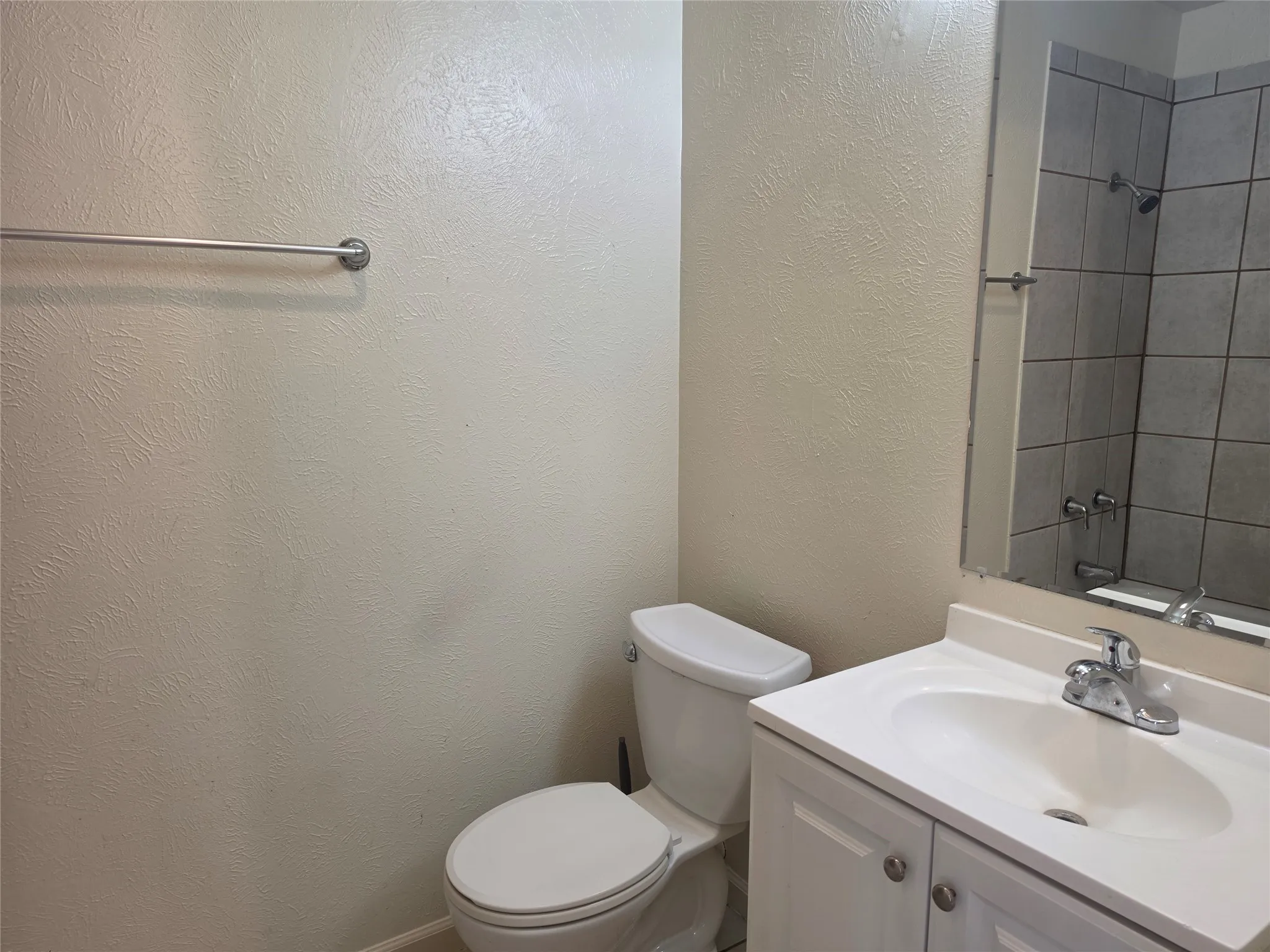 Bathroom featuring a white toilet, single vanity with integrated sink, chrome faucet, and a shower with tiled walls