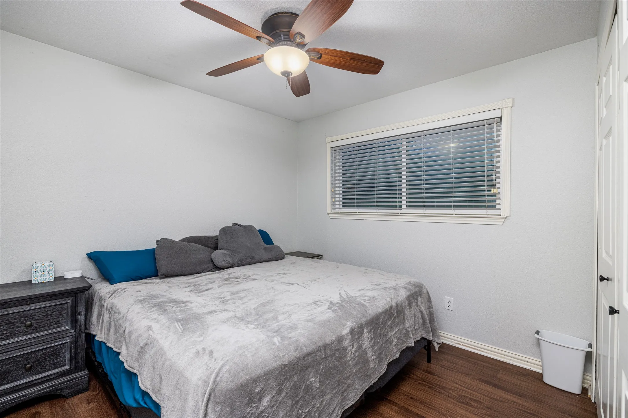 Wood-finish flooring, a ceiling fan with integrated lighting, window with blinds, and white paneled doors