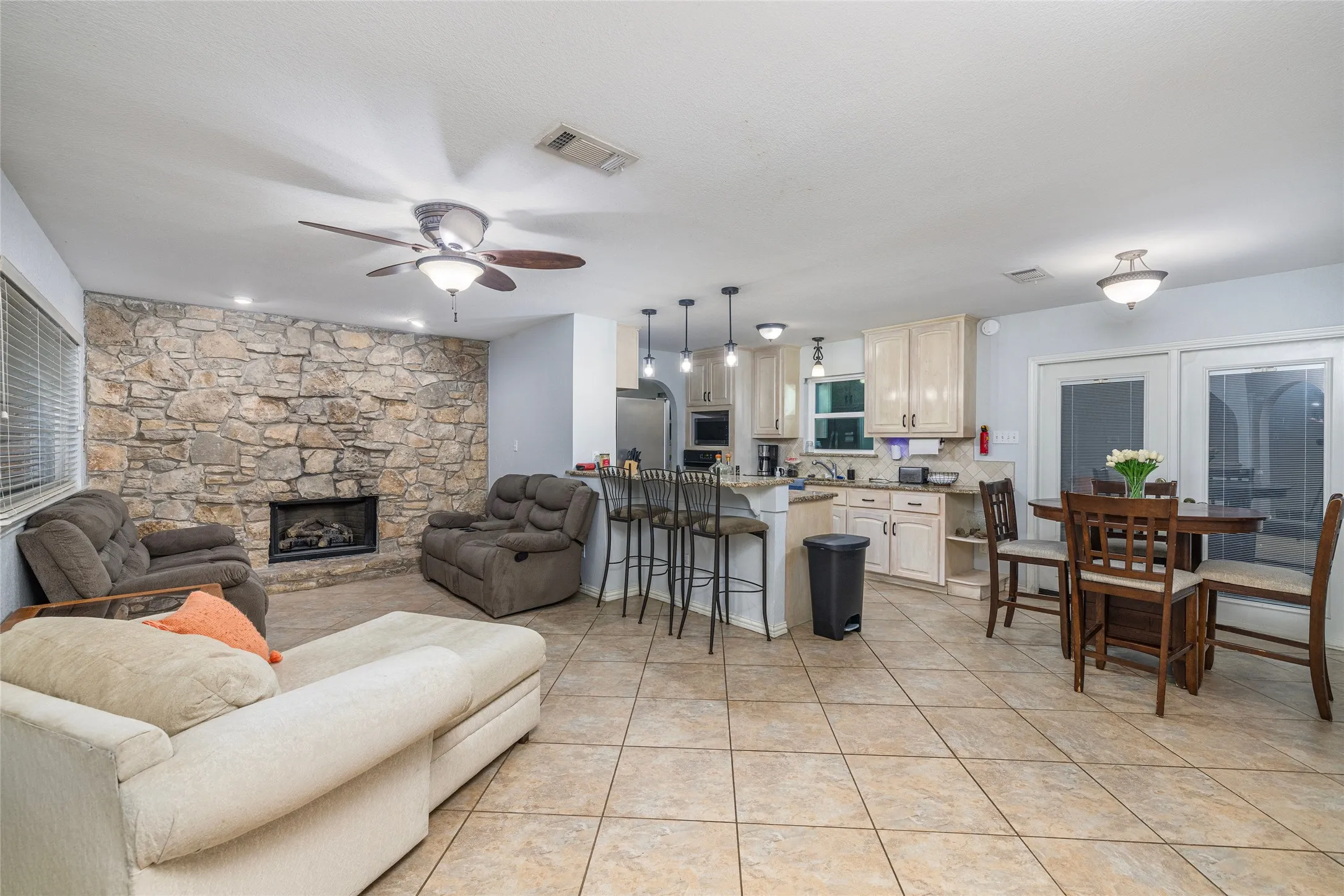 Spacious room featuring tile flooring, a stone fireplace, and a ceiling fan