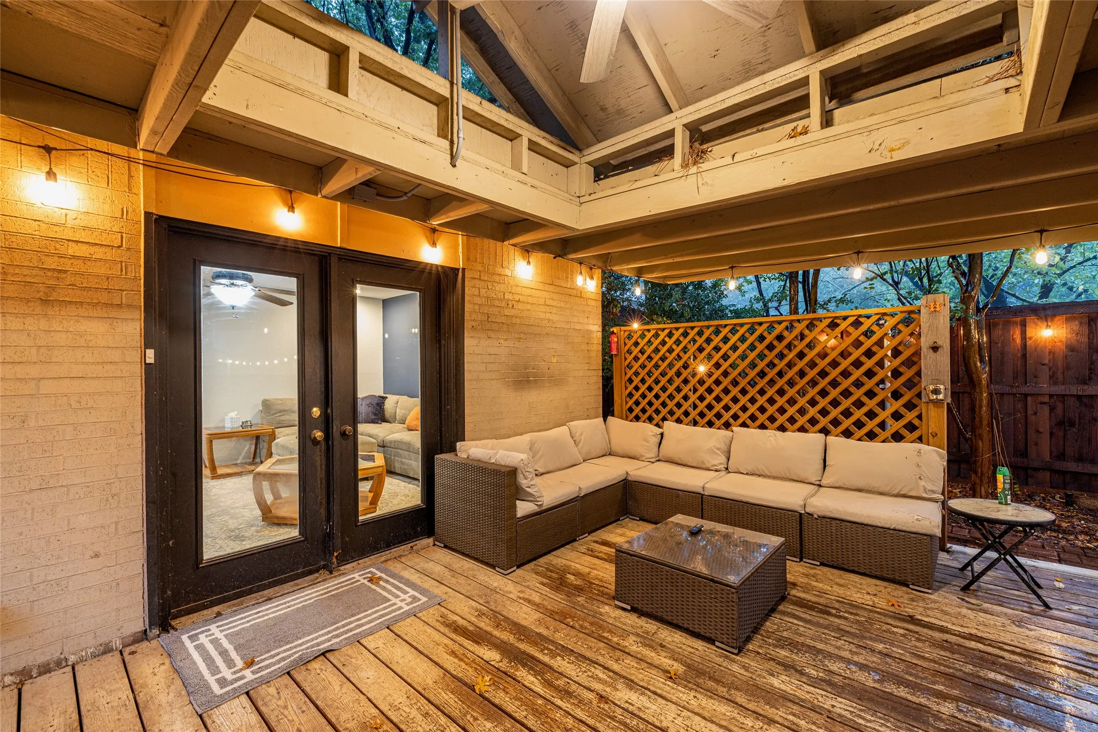 Expansive outdoor deck with wood flooring, exposed wood beam ceiling, decorative lattice privacy screen, and glass-paned French doors