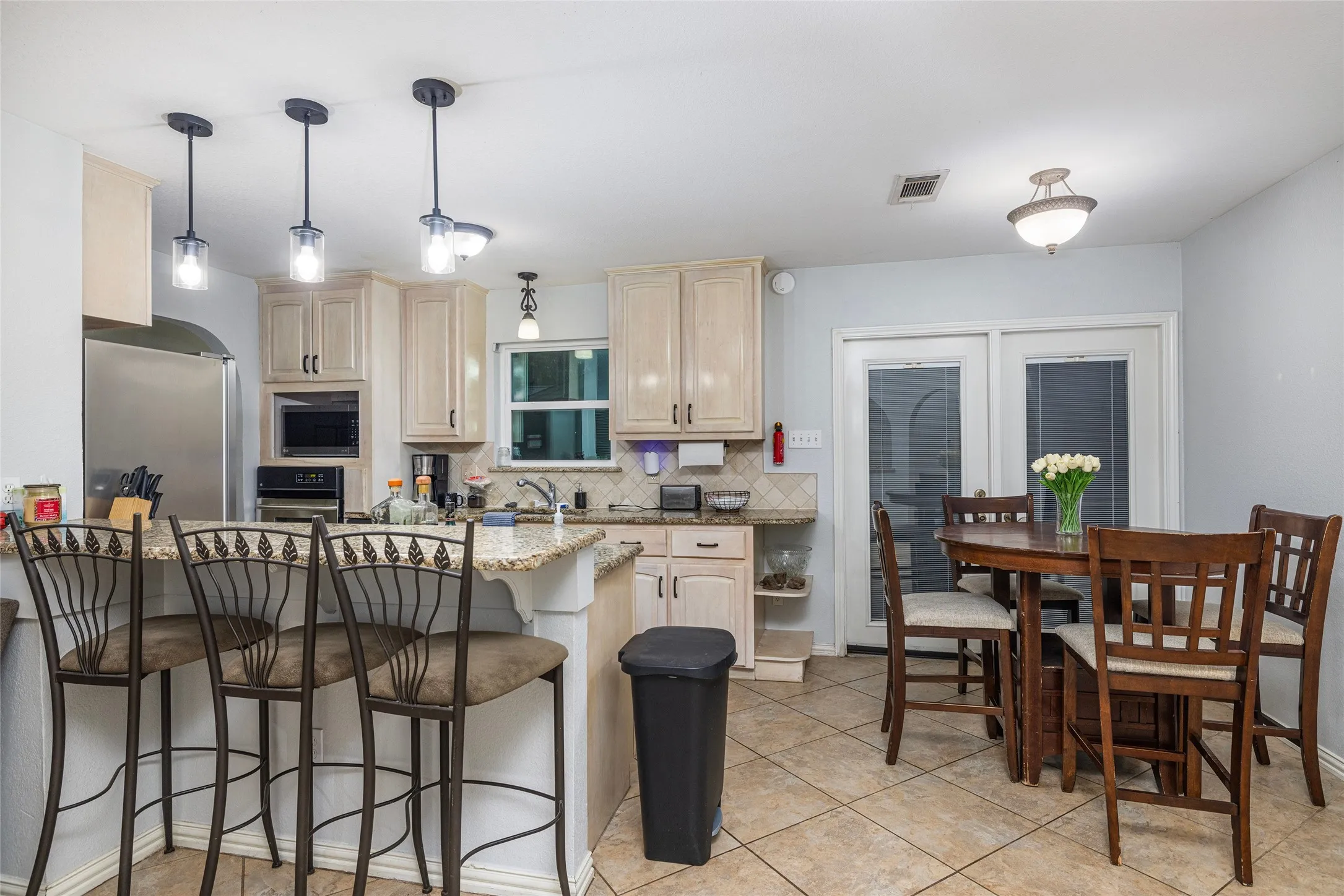 Kitchen with light cabinetry, a built-in microwave, a tile backsplash, a kitchen island with a granite-style countertop, and tile flooring