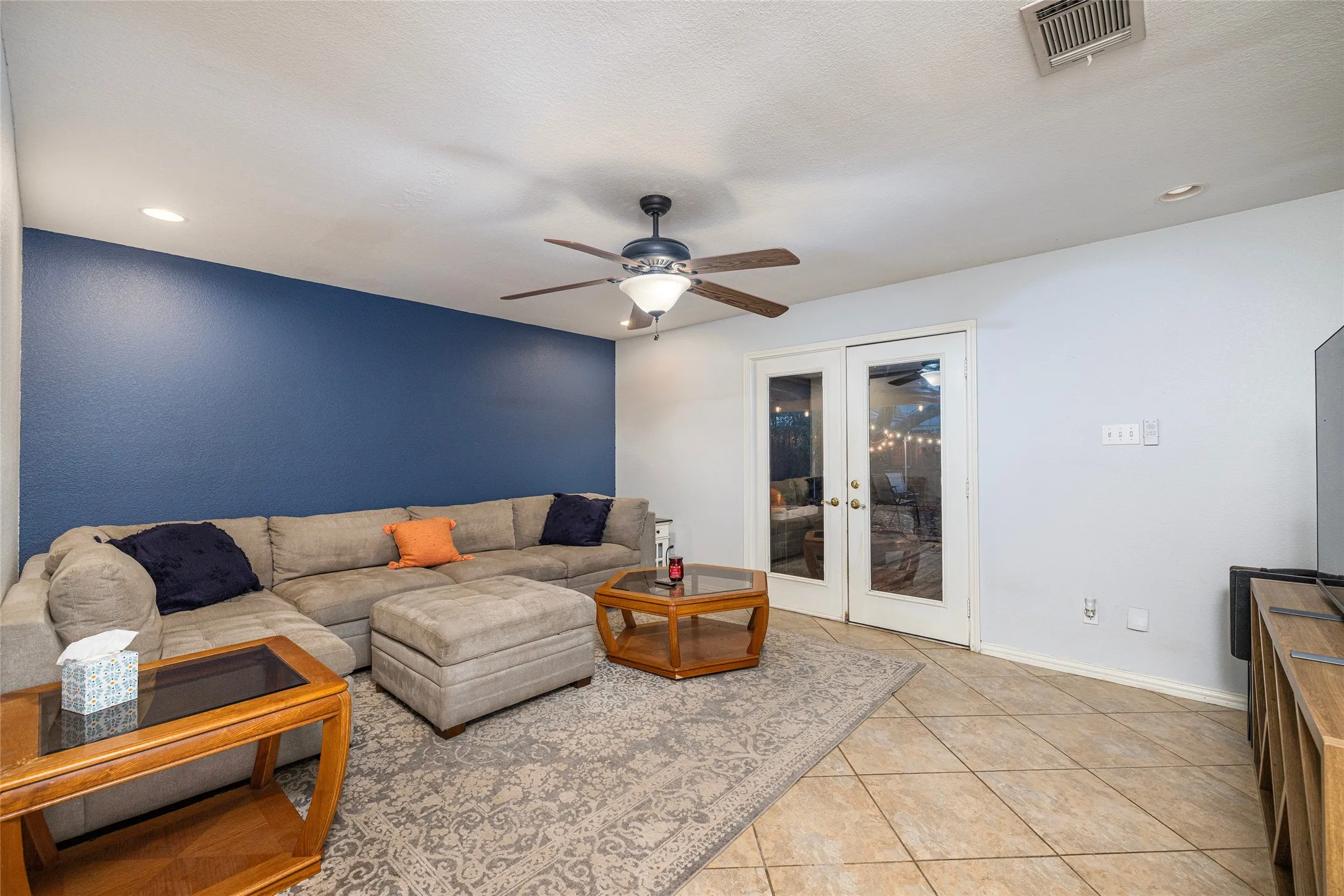 Living area featuring tile flooring, ceiling fan, and double glass-paneled doors