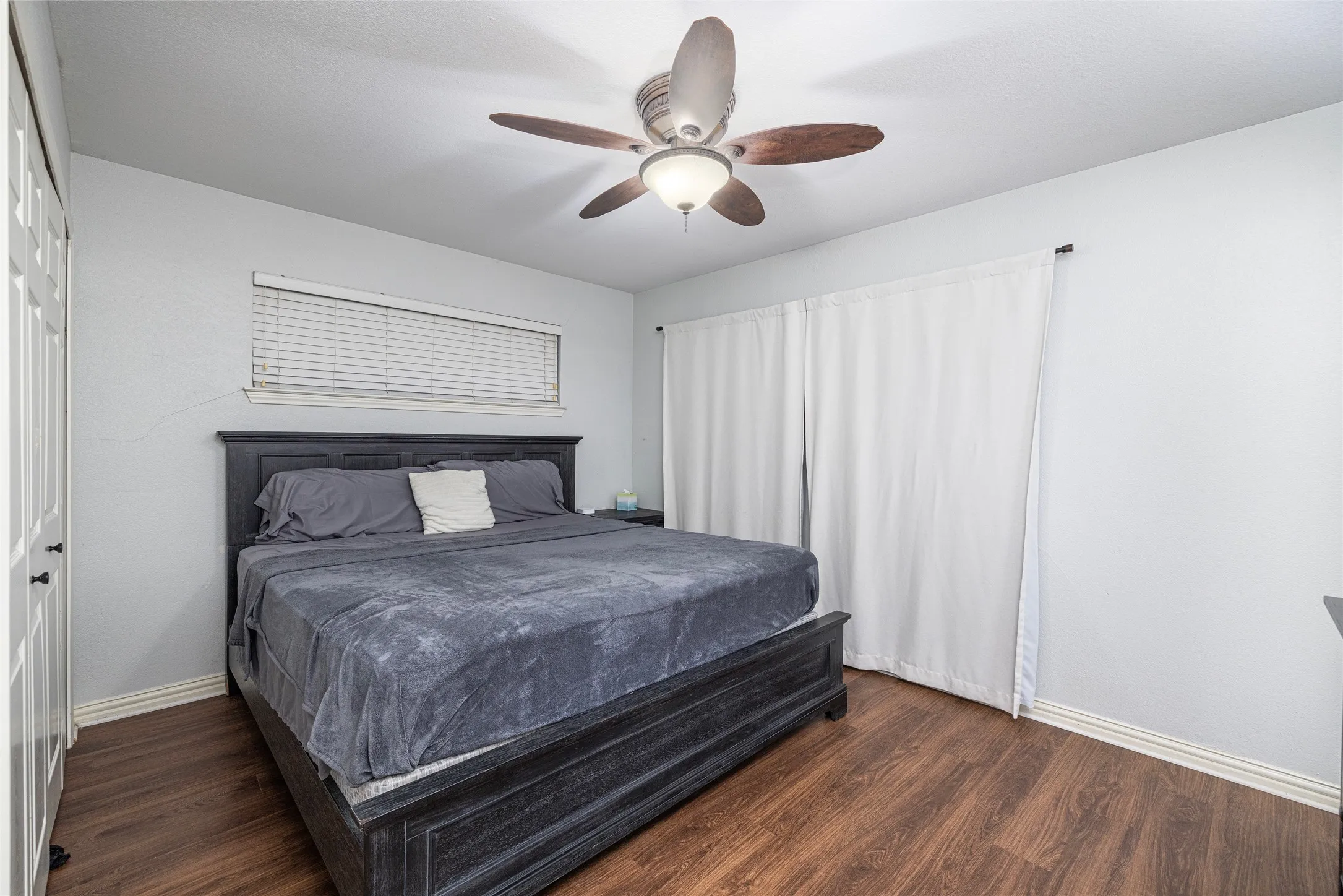 Wood-finish flooring, ceiling fan with integrated lighting, window with blinds, and white bi-fold closet doors