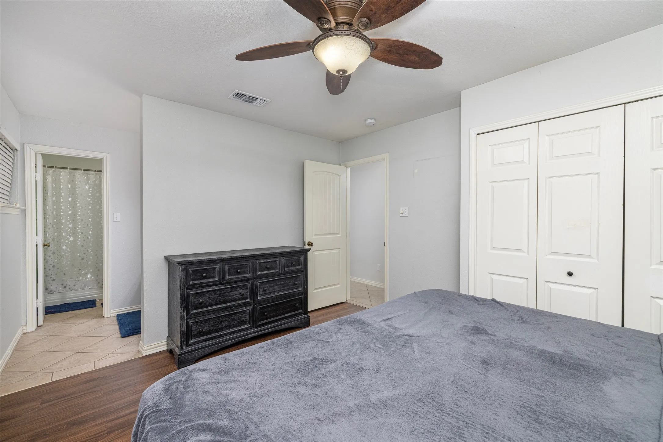 Wood-finish flooring, ceiling fan with light fixture, white bi-fold closet doors, and light gray wall paint