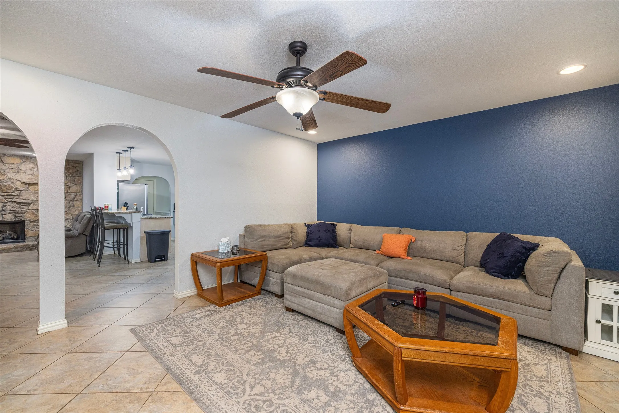 Spacious living room featuring a neutral-toned sectional layout, tile flooring, and an accent wall in deep blue