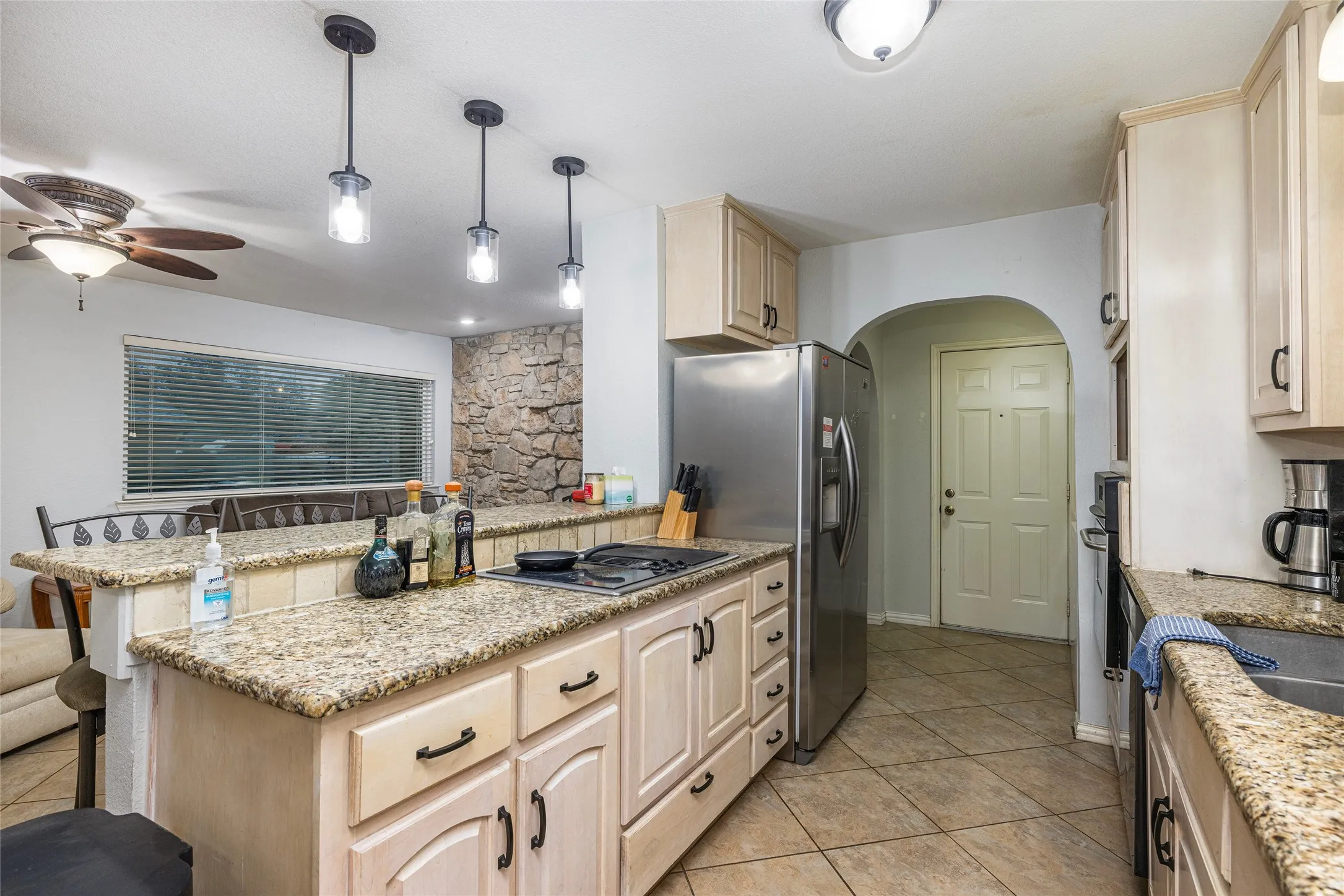 Kitchen featuring light-toned cabinetry and granite-style countertops, integrated cooktop, stainless steel refrigerator, and tiled flooring
