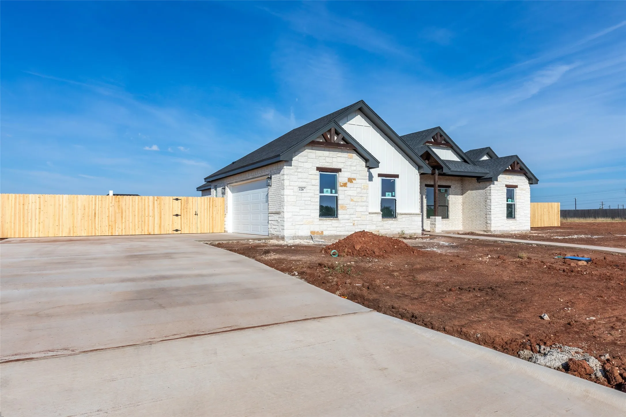 Stone and siding exterior with dark-framed windows, a dark shingled roof, an attached garage, and a concrete driveway