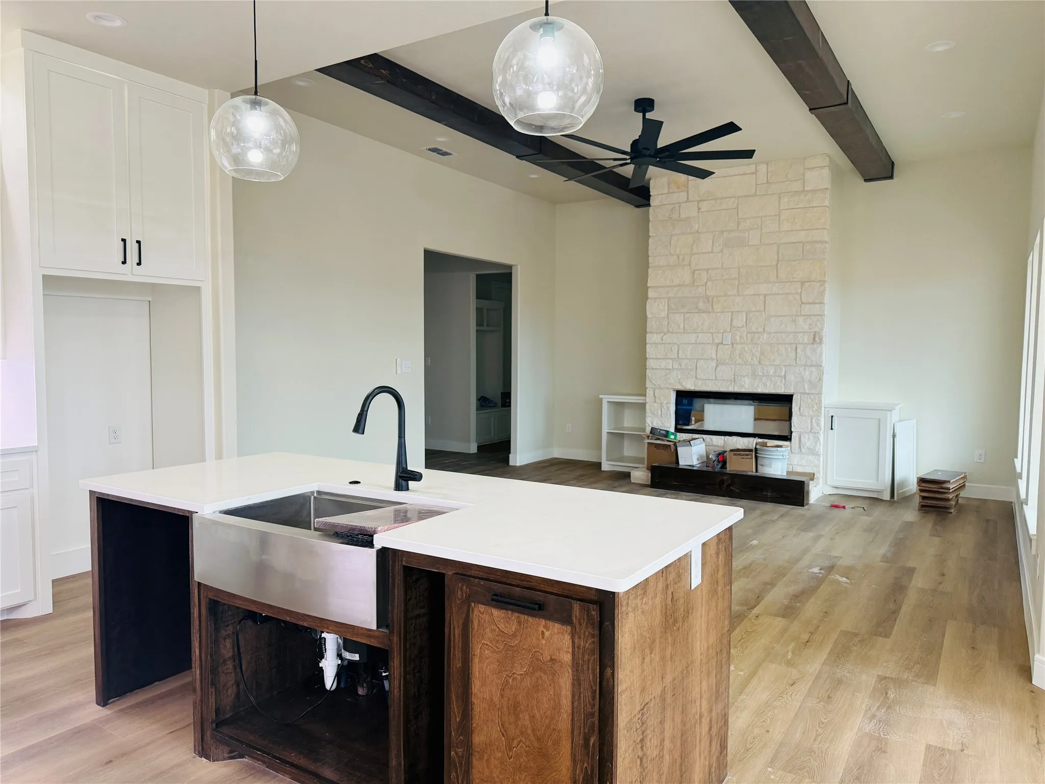 Kitchen island with a stainless steel farmhouse sink and matte black faucet, quartz countertops, wood-finish flooring, and a stone-clad fireplace with wood beams