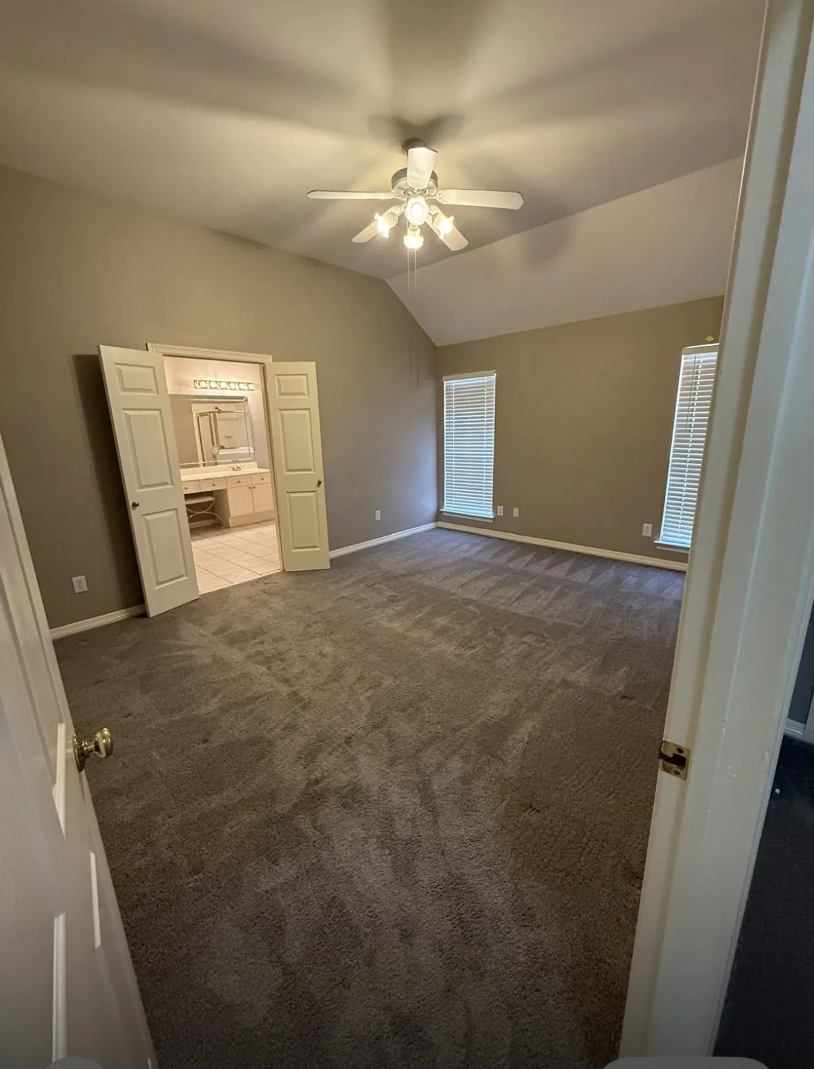 Unfurnished bedroom with connected bathroom, carpet floors, ceiling fan, and vaulted ceiling