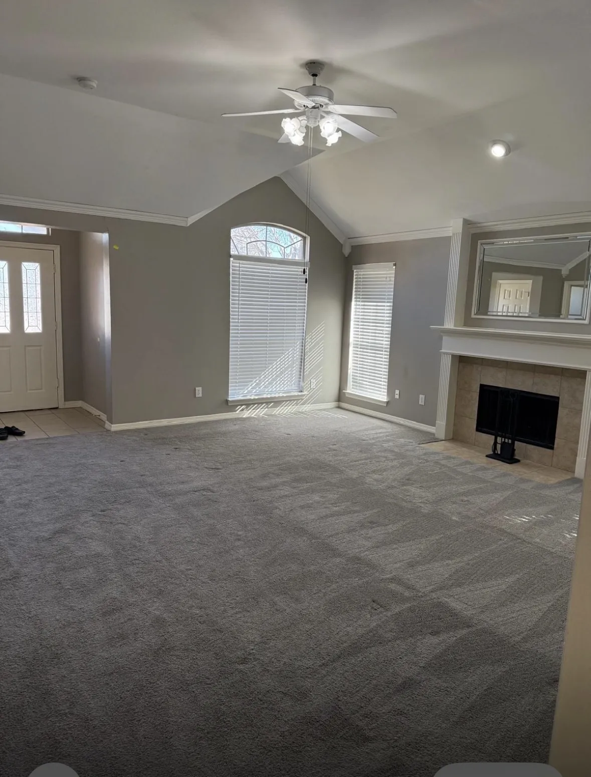Unfurnished living room featuring a tile fireplace, ceiling fan, carpet floors, ornamental molding, and vaulted ceiling
