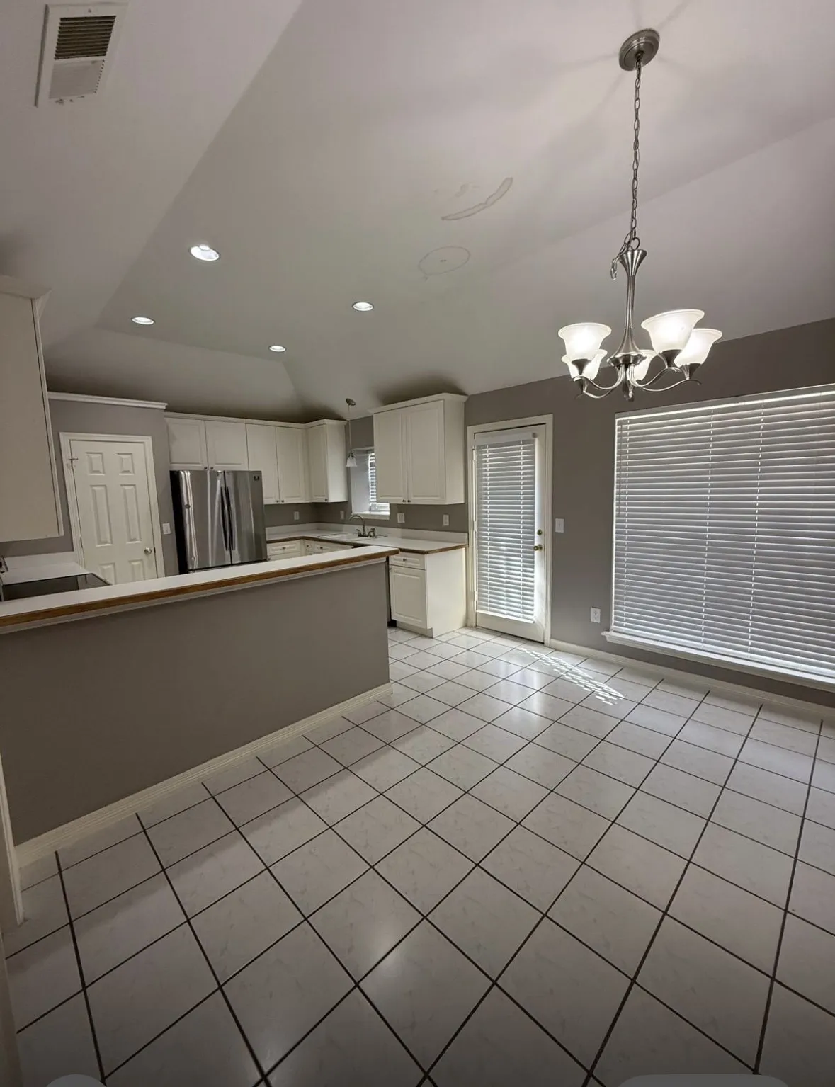Kitchen with light tile patterned flooring, pendant lighting, white cabinetry, lofted ceiling, and stainless steel fridge