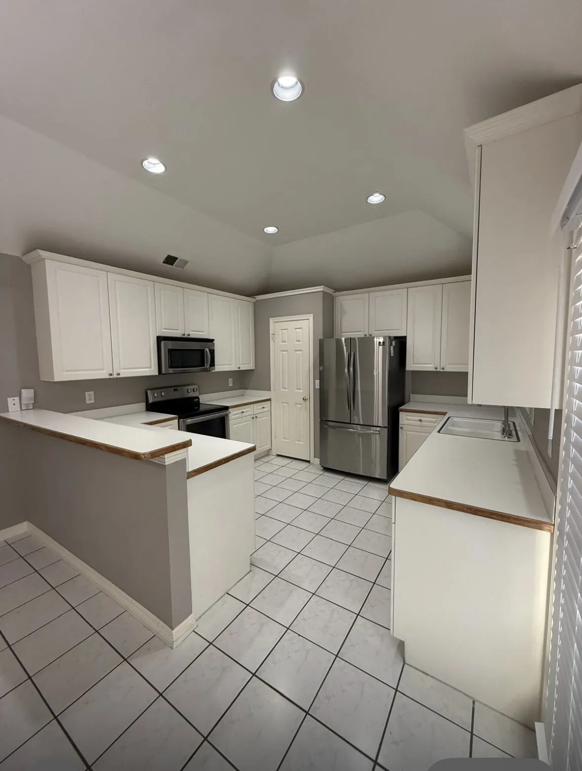 Kitchen with lofted ceiling, appliances with stainless steel finishes, kitchen peninsula, and white cabinets