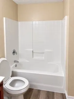 Bathtub with white surround and integrated grab bar, chrome fixtures, and wood-finish flooring