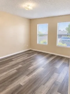 Wood-finish flooring, two windows with blinds, flush mount ceiling light, and neutral wall paint