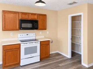 Wood-finish flooring, wood cabinetry, white countertops, built-in microwave, and a pantry with wire shelving