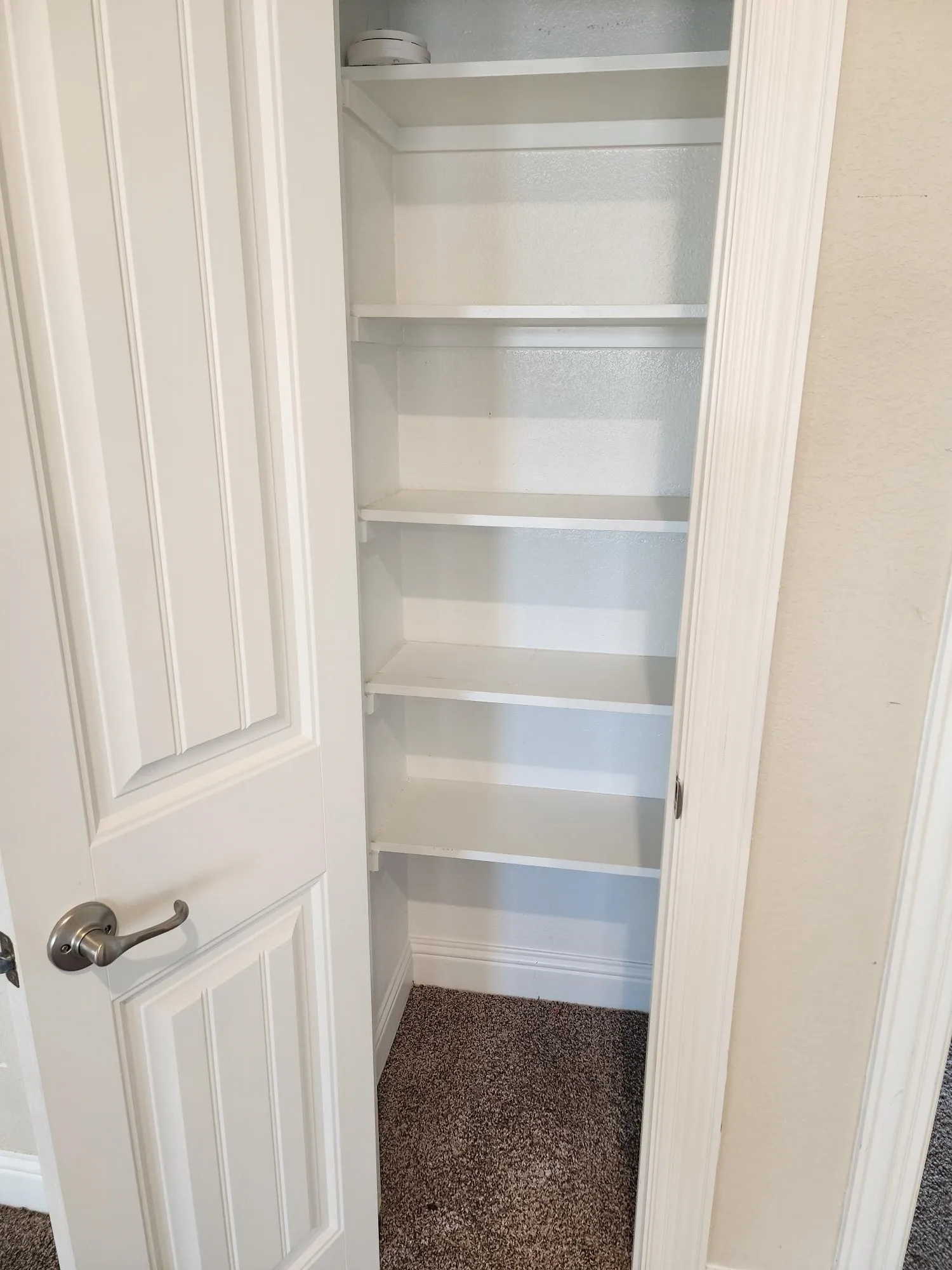 Built-in shelving with multiple levels, paneled interior door, satin nickel door hardware, and textured wall finish