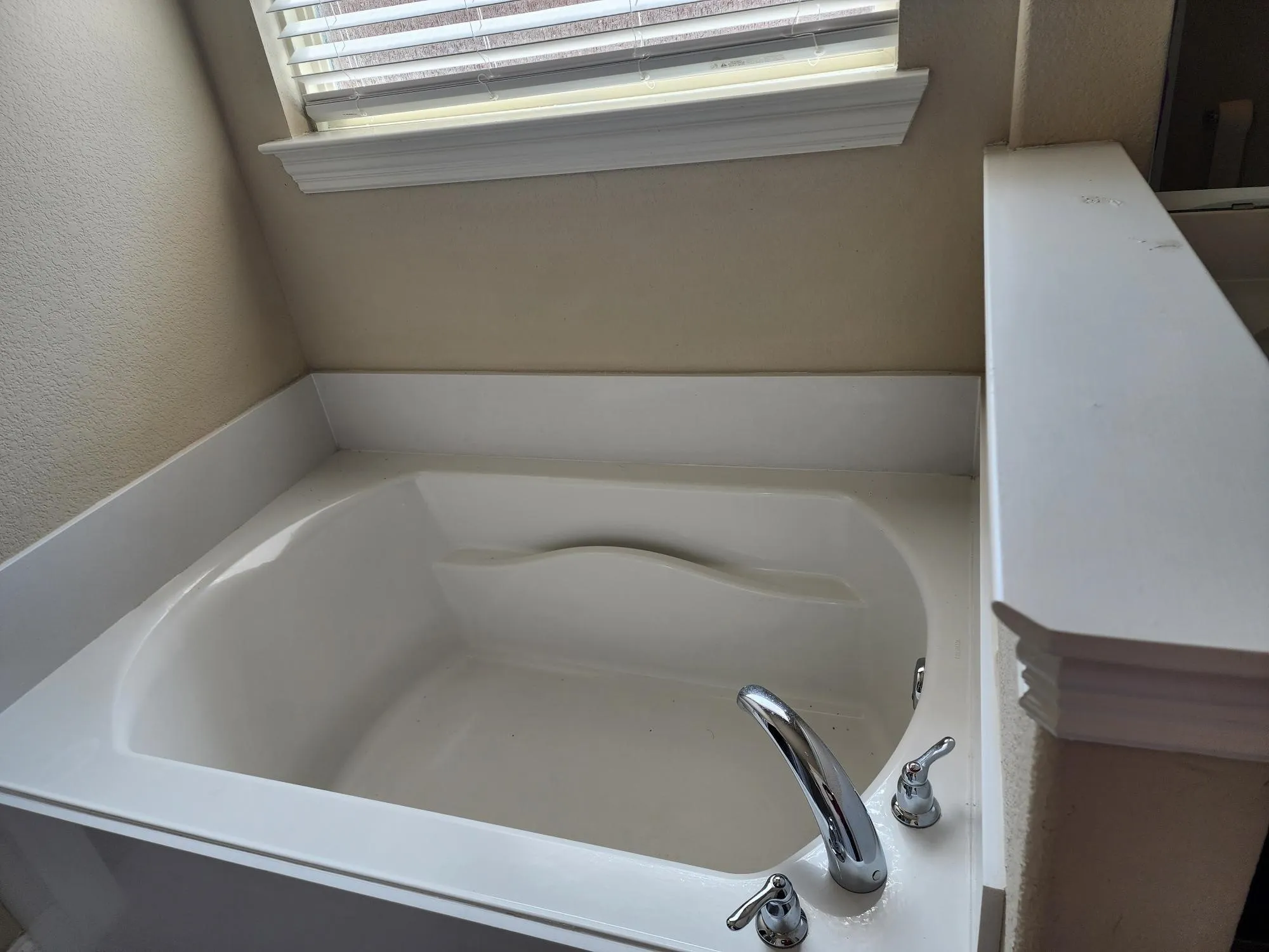 Built-in soaking tub with chrome fixtures and a window with blinds