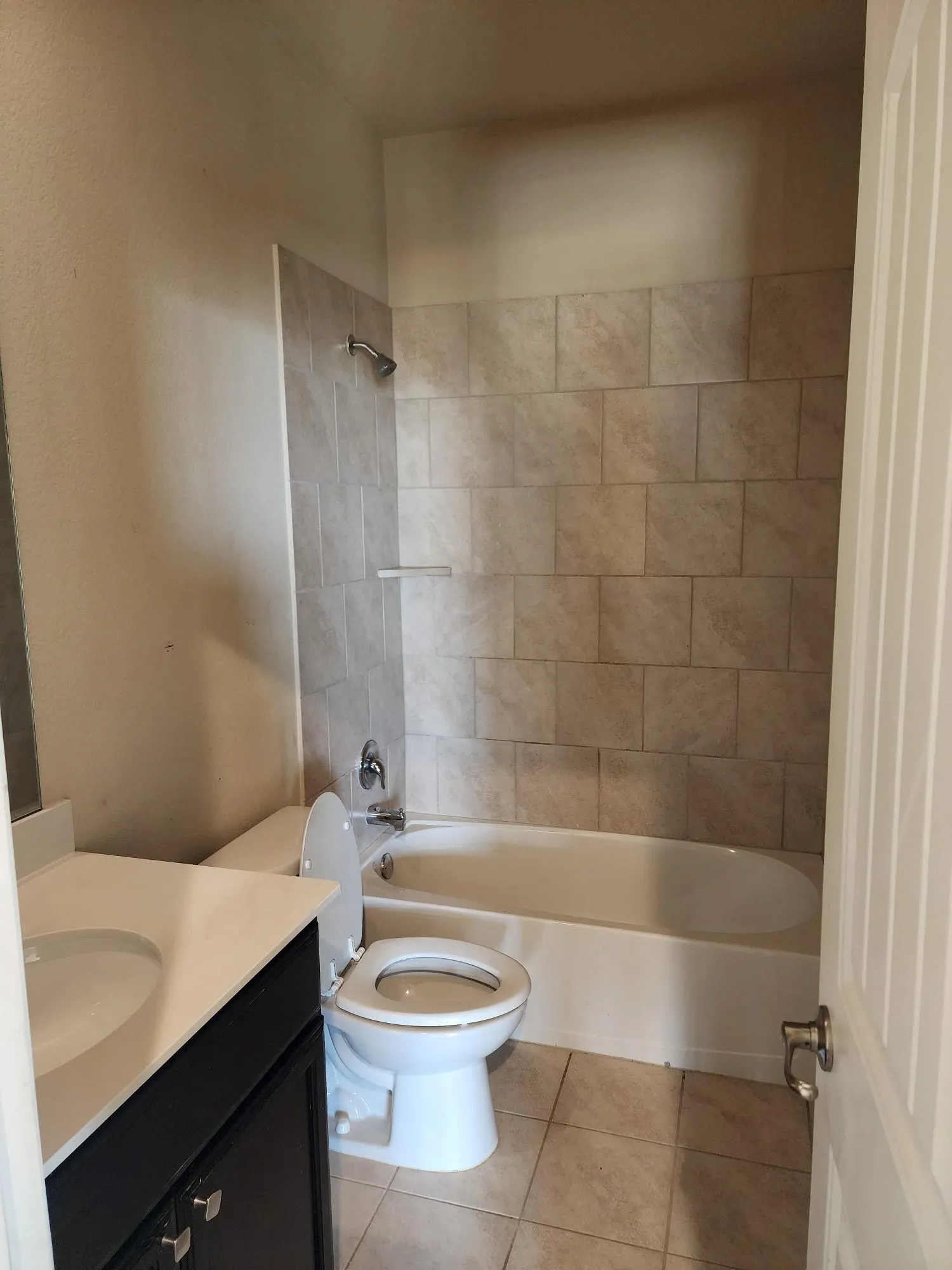 Bathroom featuring a porcelain tub with tiled surround, a toilet, a vanity with an integrated sink, and tiled flooring