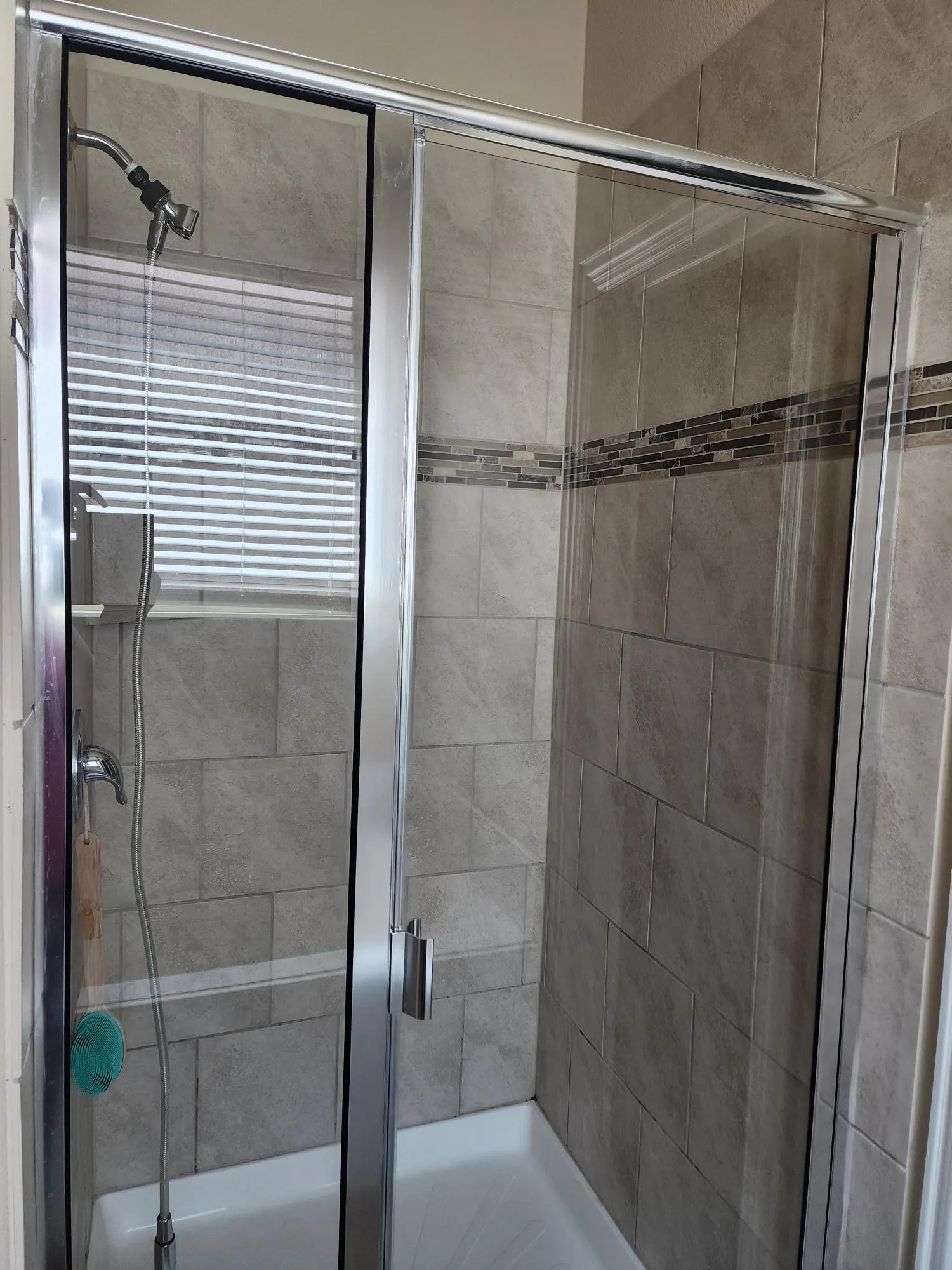 Modern frameless glass shower enclosure featuring chrome hardware, ceramic tile surround with decorative border accent, and a sleek showerhead with handheld spray fixture