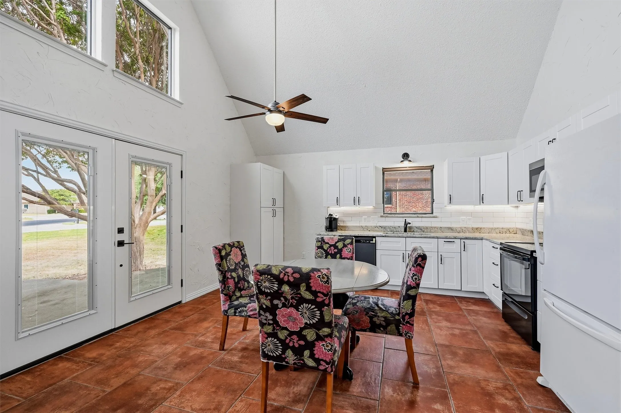 Vaulted ceiling with a ceiling fan, white cabinetry with under-cabinet lighting, tile flooring, glass panel double doors