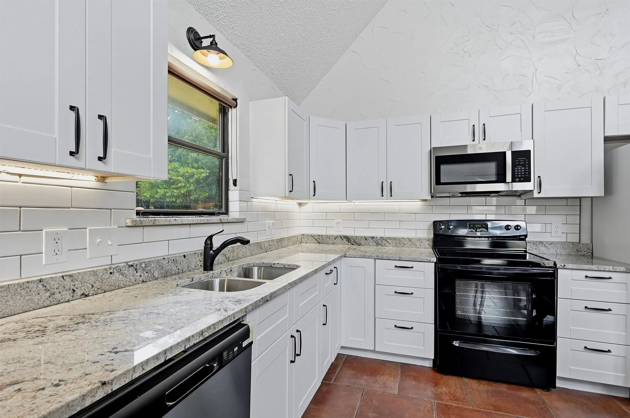 Contemporary kitchen featuring white cabinetry, granite countertops, a stainless steel microwave, black range, and white subway tile backsplash