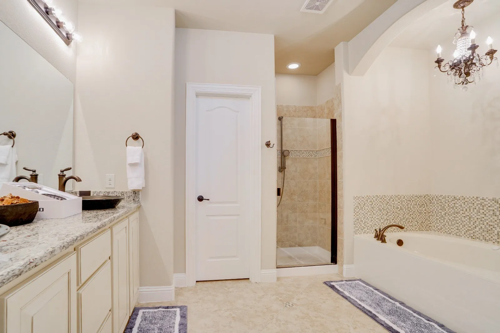 Dual vanity with integrated sinks, a tiled walk-in shower, a built-in soaking tub, and a decorative chandelier