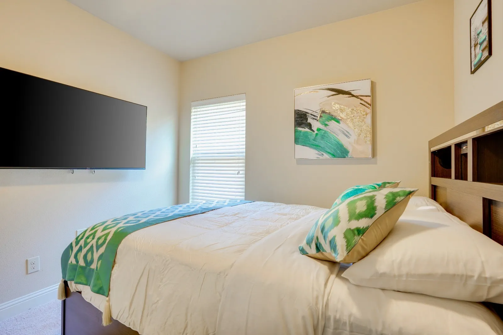 Wall-mounted television, window with blinds, and built-in headboard storage