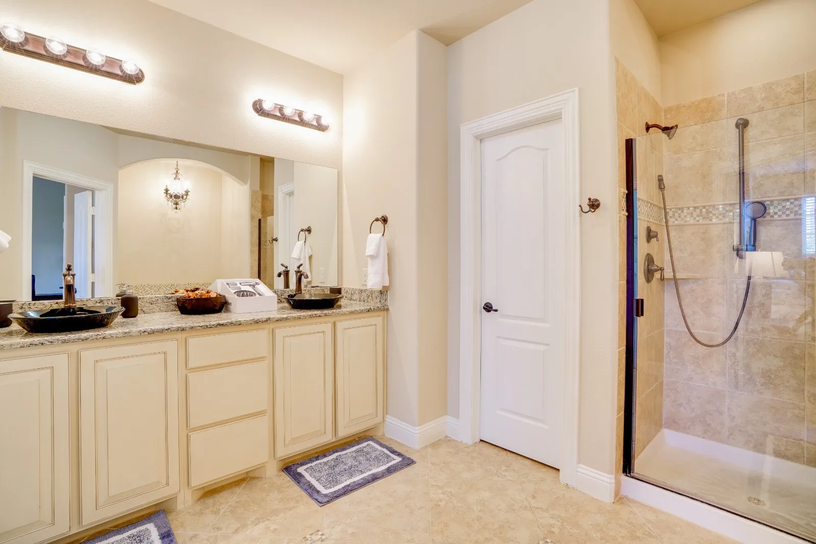 Dual vessel sinks, granite-finish countertop, extensive vanity with cabinetry, tile flooring, and a glass-enclosed shower