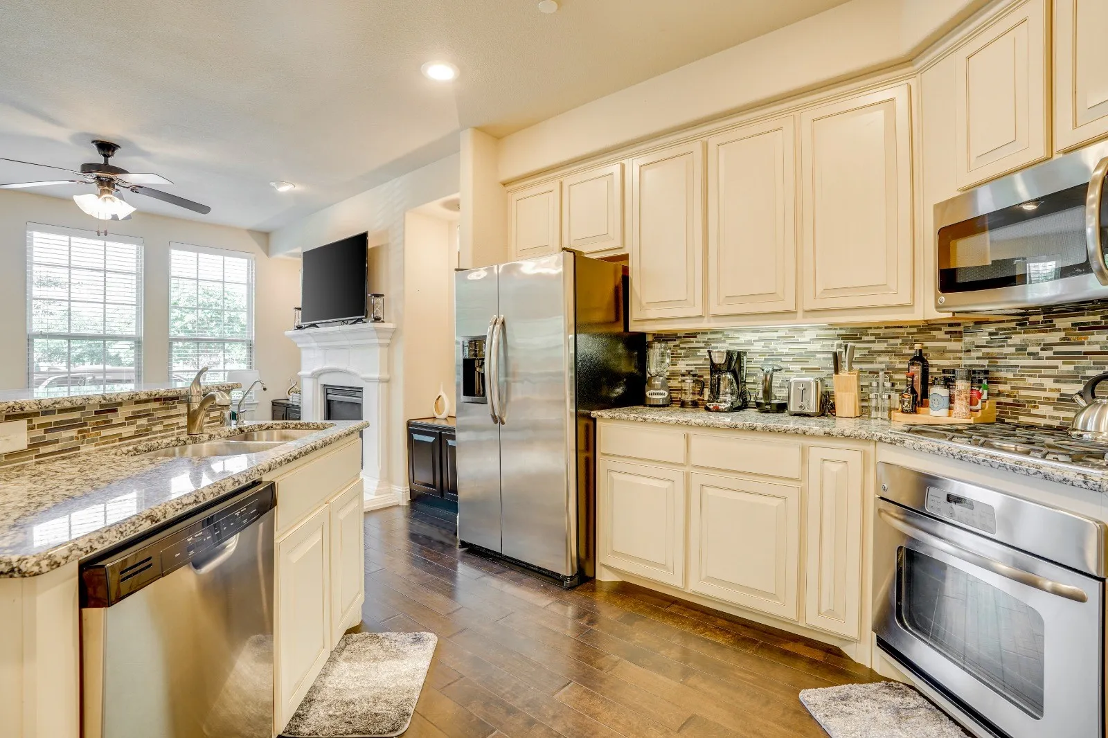 Kitchen featuring stainless steel appliances, light-toned cabinetry, granite countertops, and a mosaic tile backsplash