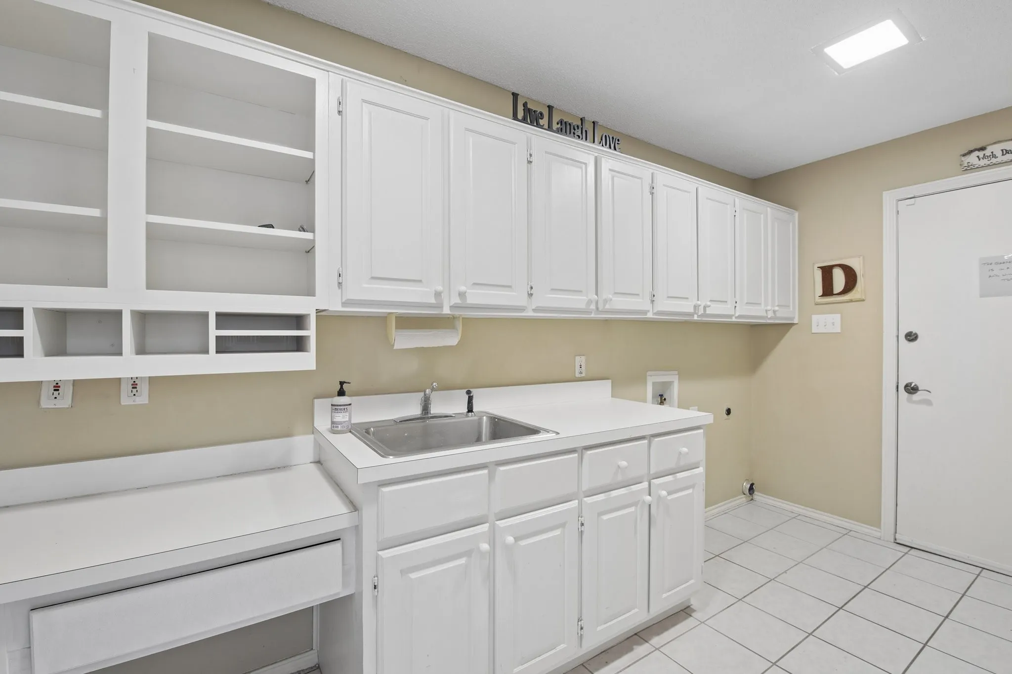 White cabinetry with abundant storage, stainless steel sink, expansive white countertops, integrated desk area, and ceramic tile flooring