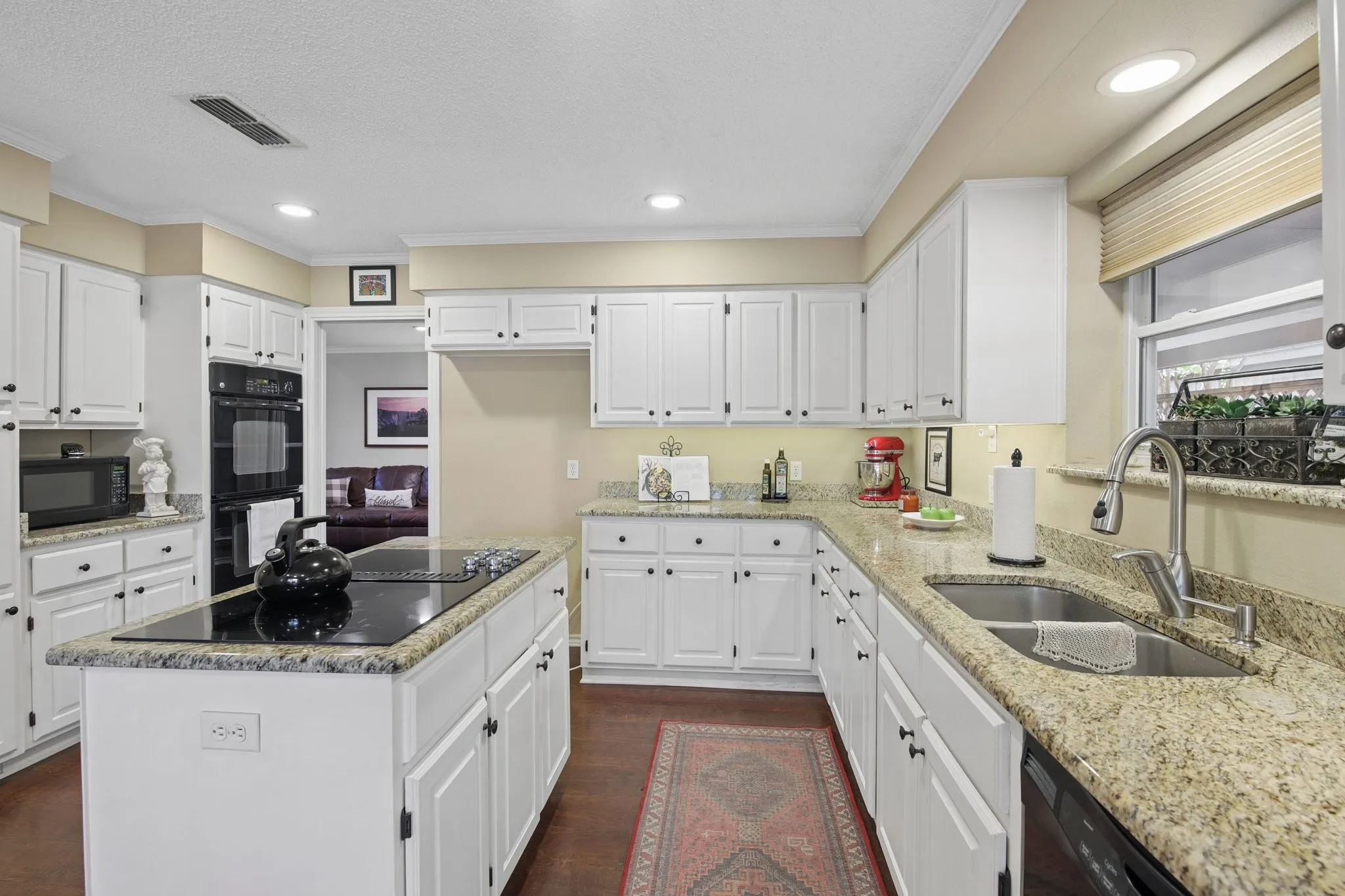 Kitchen featuring double oven, island cooktop, white cabinets, granite countertops, a double basin stainless steel sink