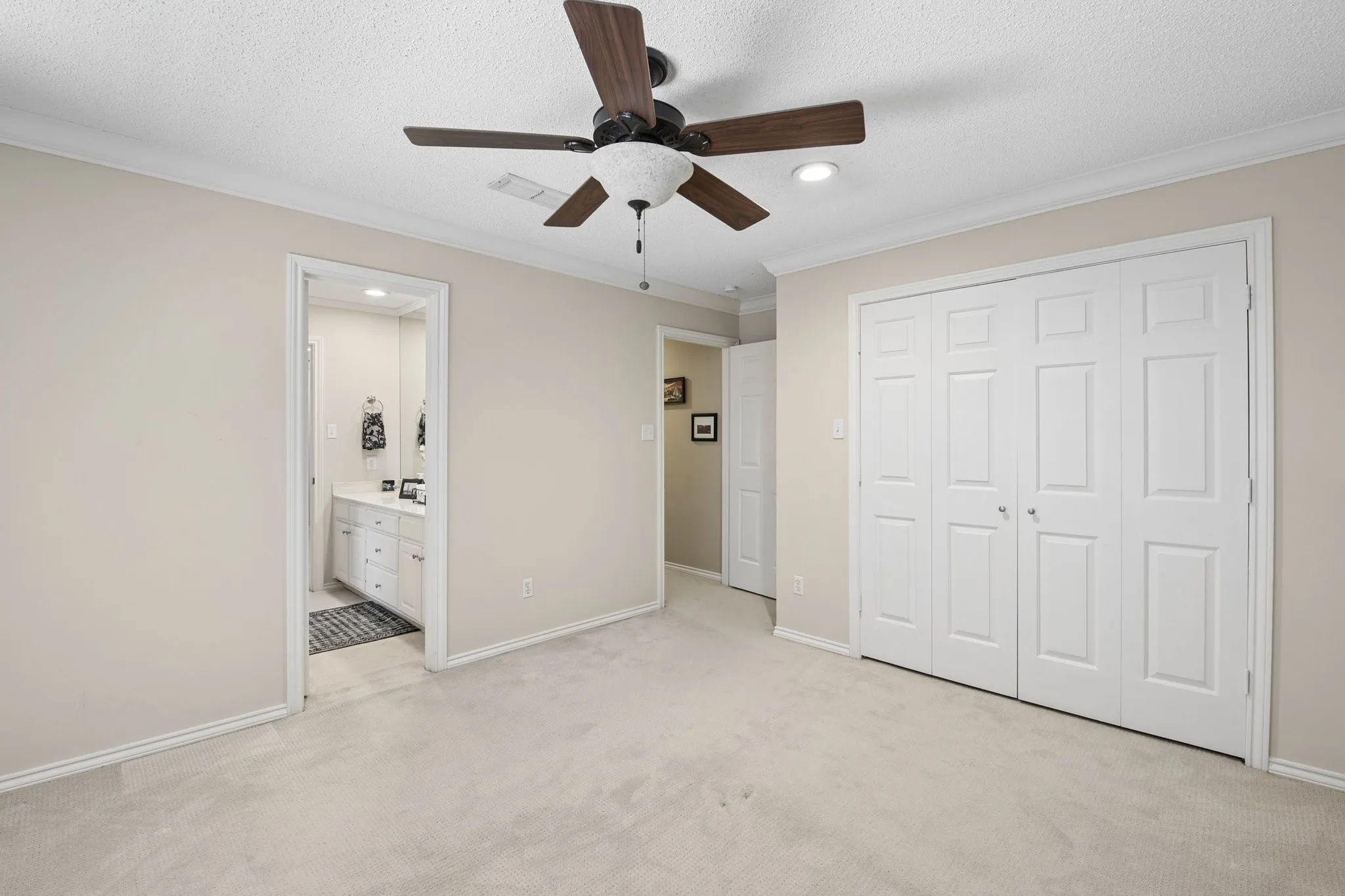 Recessed lighting, ceiling fan with wood-finish blades, crown molding, white paneled bifold doors, and an attached bathroom featuring a double vanity