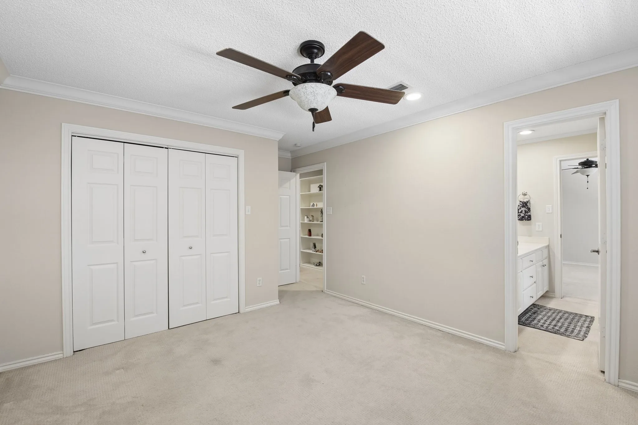 Neutral tone wall paint, crown molding, ceiling fan with integrated lighting, carpeted flooring, and bi-fold closet doors