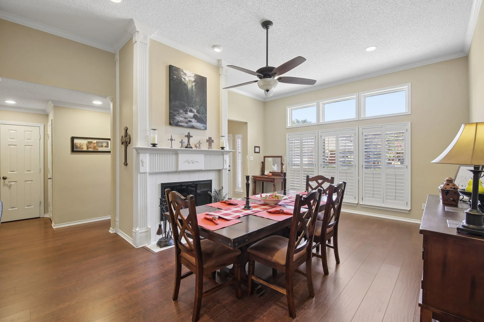 Hardwood flooring, white fireplace mantel with decorative columns, white plantation shutters, ceiling fan with light fixture, and recessed lighting