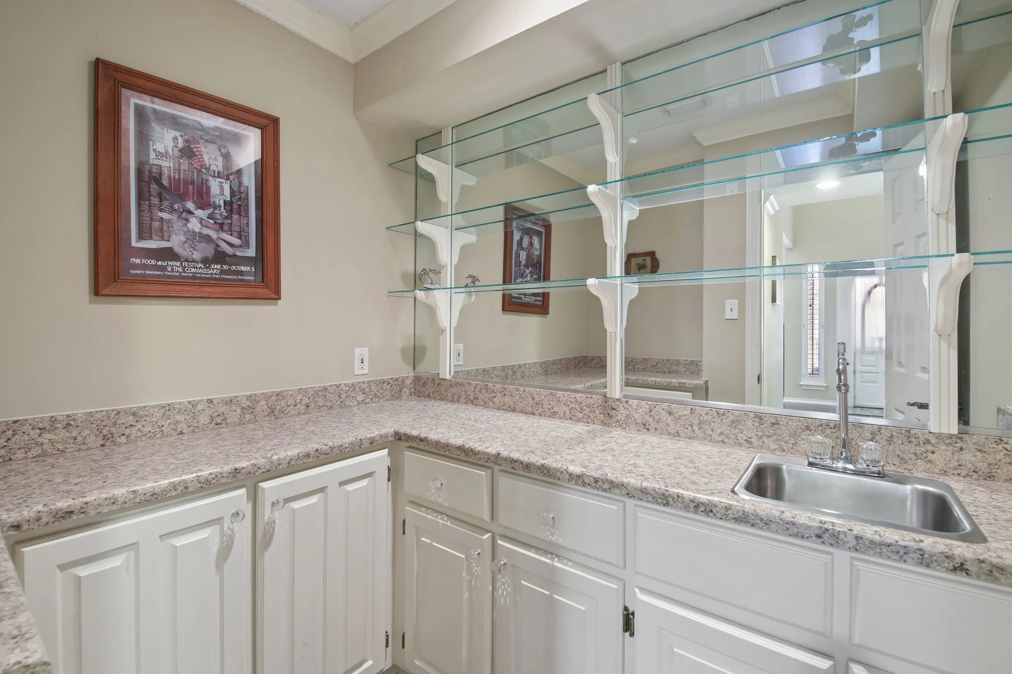 Built-in wet bar featuring white cabinetry, speckled countertops, a stainless steel sink, and mirrored backsplash with glass shelving