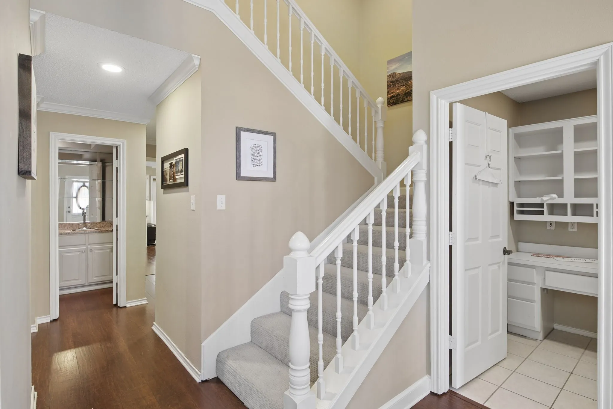 Wood-finish flooring, staircase with carpeted treads and white balusters, built-in desk with shelving, recessed lighting, and crown molding