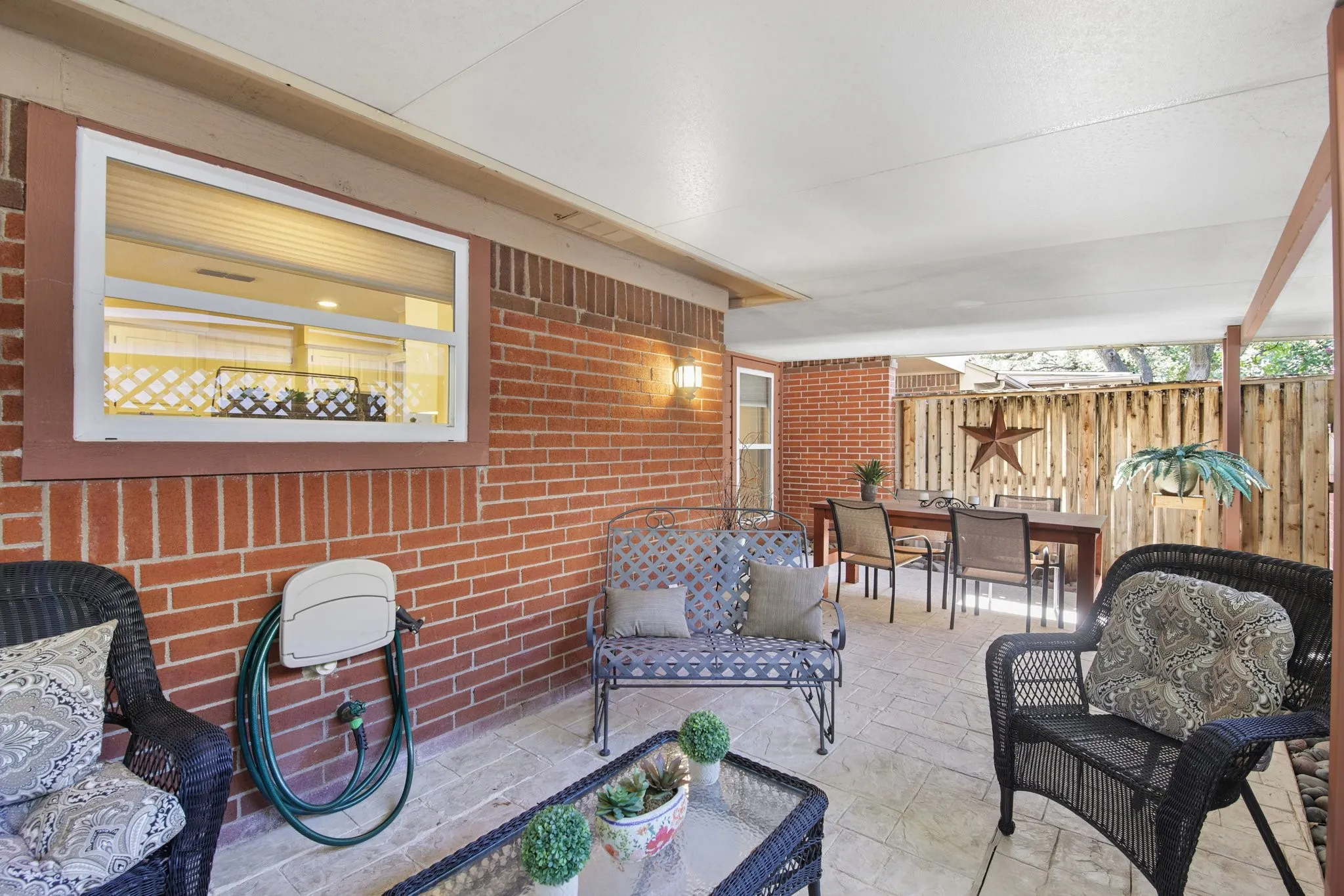 Covered patio featuring a brick exterior, stamped concrete flooring, a privacy fence, and an exterior wall sconce