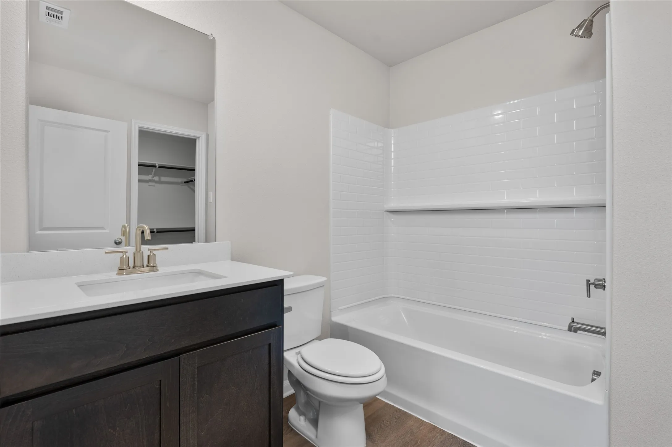 Bathroom featuring  shower combination, vanity, dark wood-style flooring, and a spacious closet