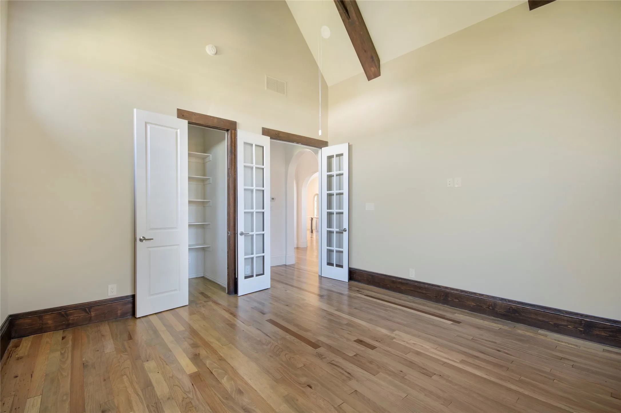 Vaulted ceiling with exposed wood beams, wood-finish flooring, white panel door, white French doors, and built-in shelving