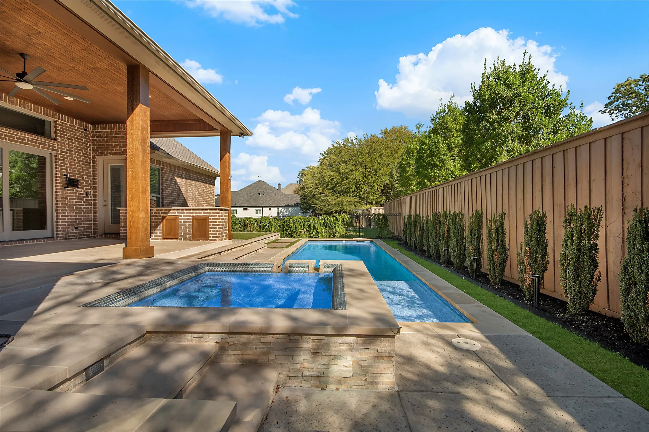 Expansive outdoor area featuring a swimming pool, integrated spa, and a covered patio with a wood-finish ceiling and a ceiling fan