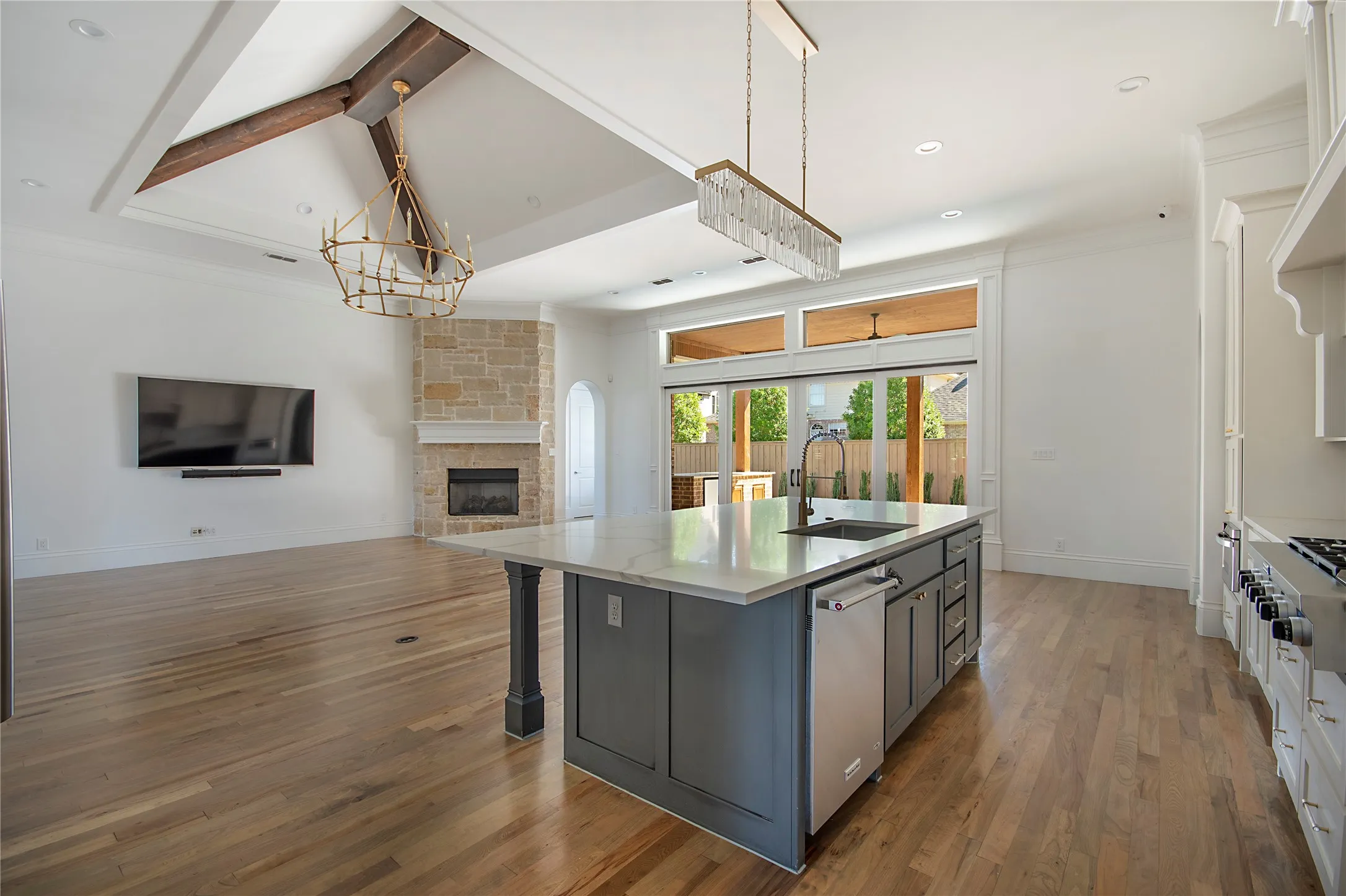 Open-concept area featuring hardwood flooring, a stone fireplace, and a kitchen island with a built-in sink and dishwasher